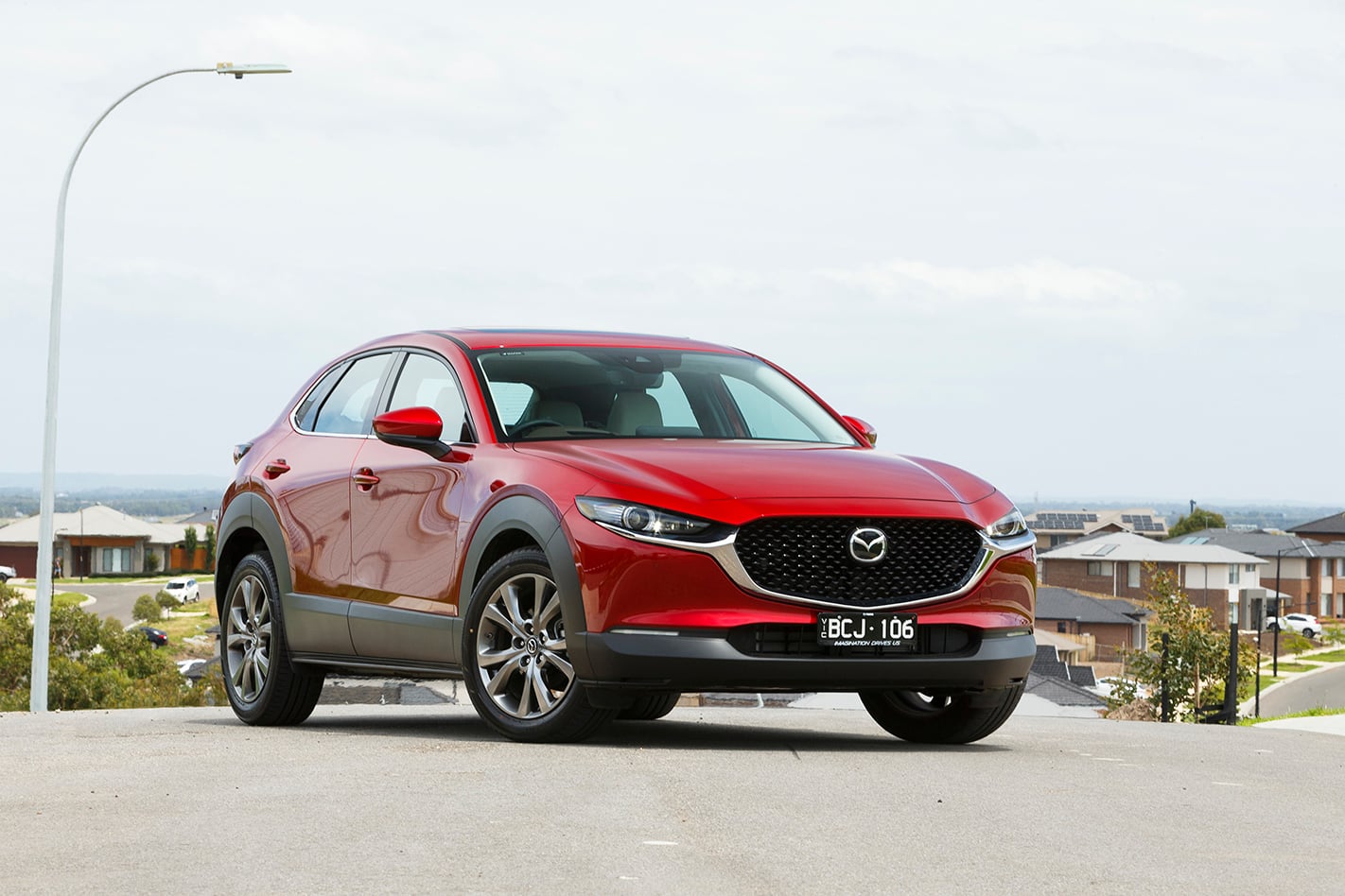 Red Mazda SUV (CX-5) parked on a suburban street with houses in the background, front three-quarter view, daylight.