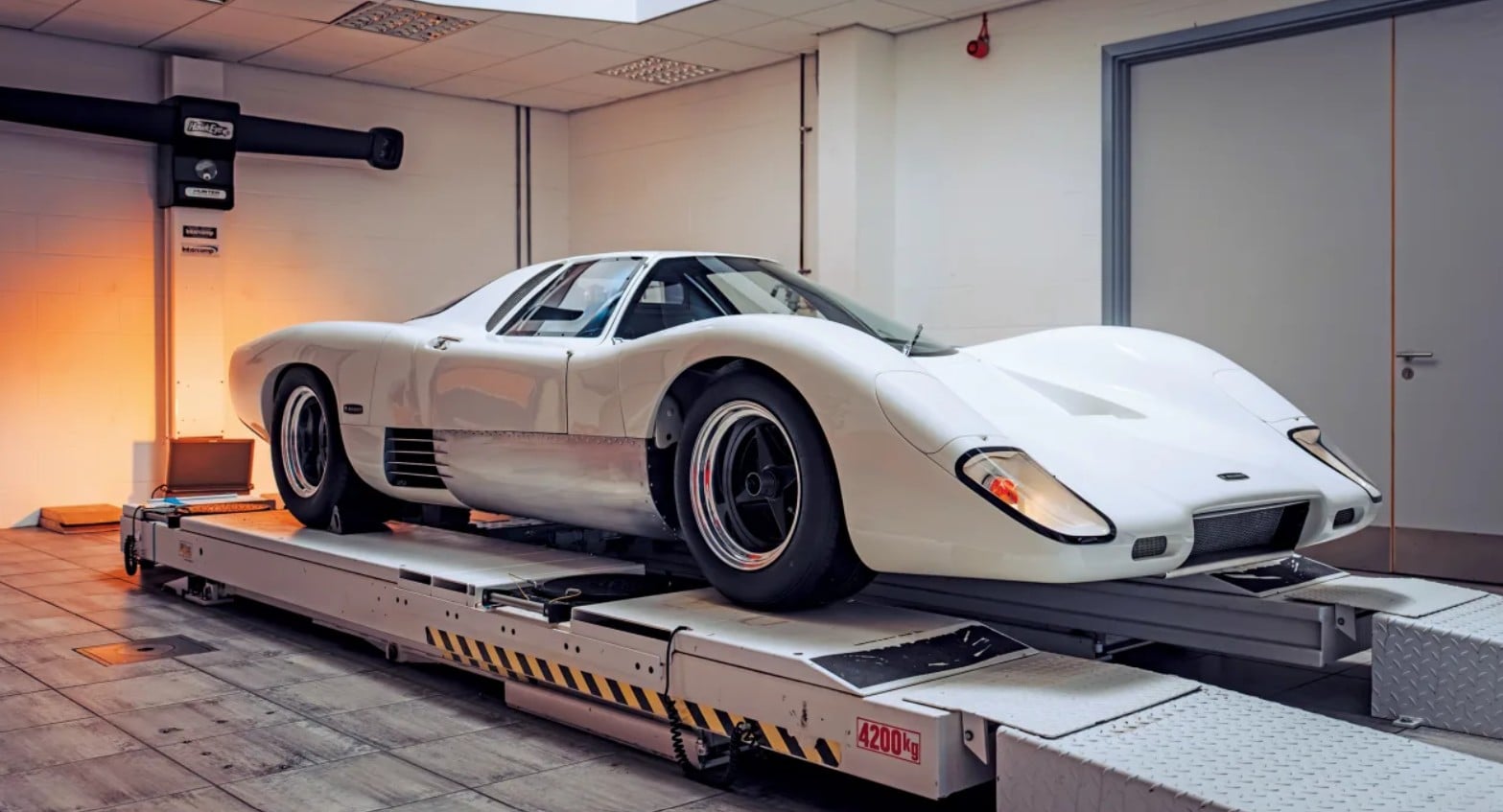 White vintage sports car on a rolling test platform inside a garage or lab, ready for diagnostics or testing.