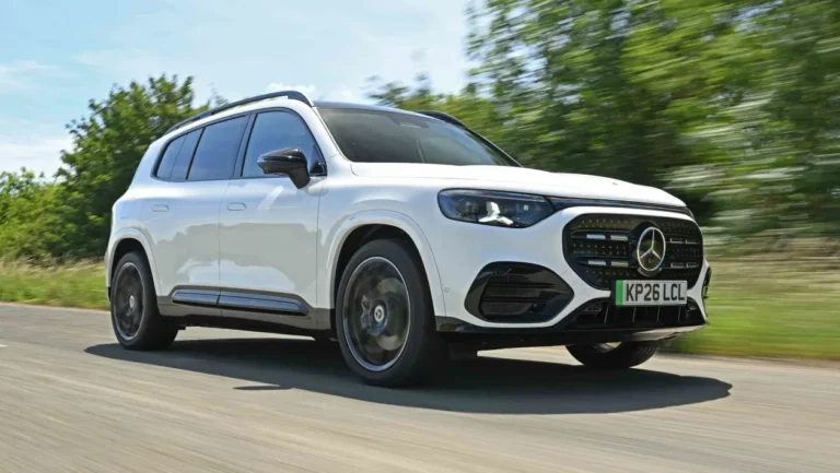 White Mercedes-Benz SUV driving on a tree-lined road, front grille visible and motion blur indicating speed.