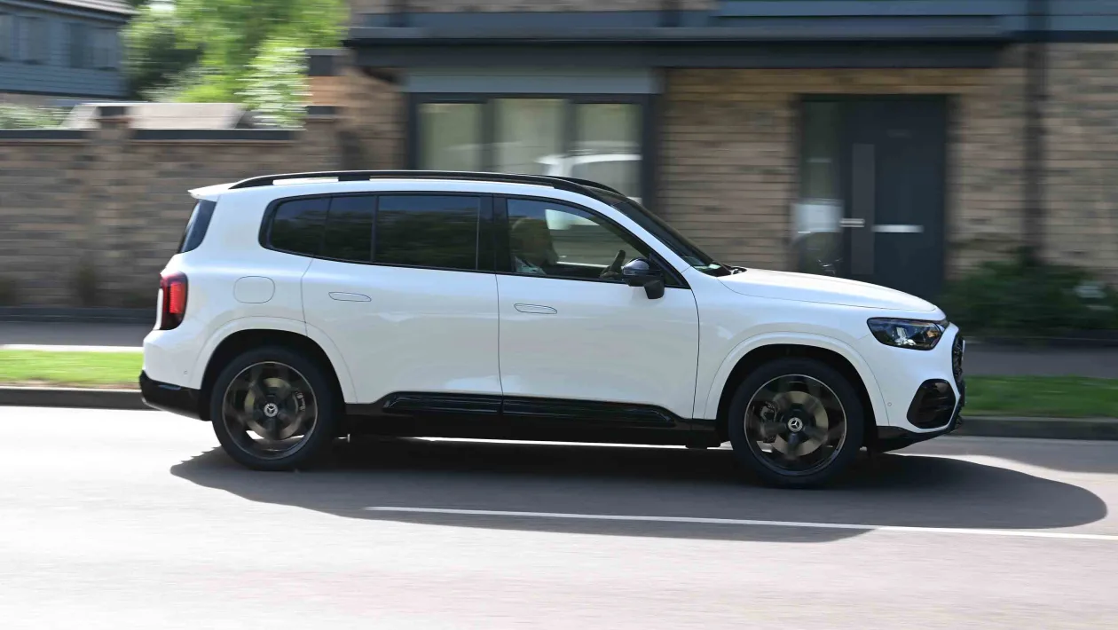 White SUV driving on a suburban street, side view, under clear daylight.