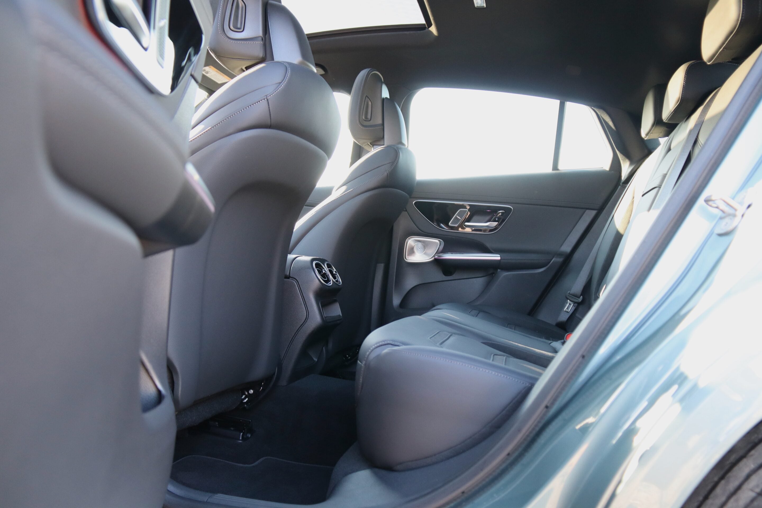 Rear passenger area of a sedan with black leather seats, visible headrests, and door panel settings along the side window.