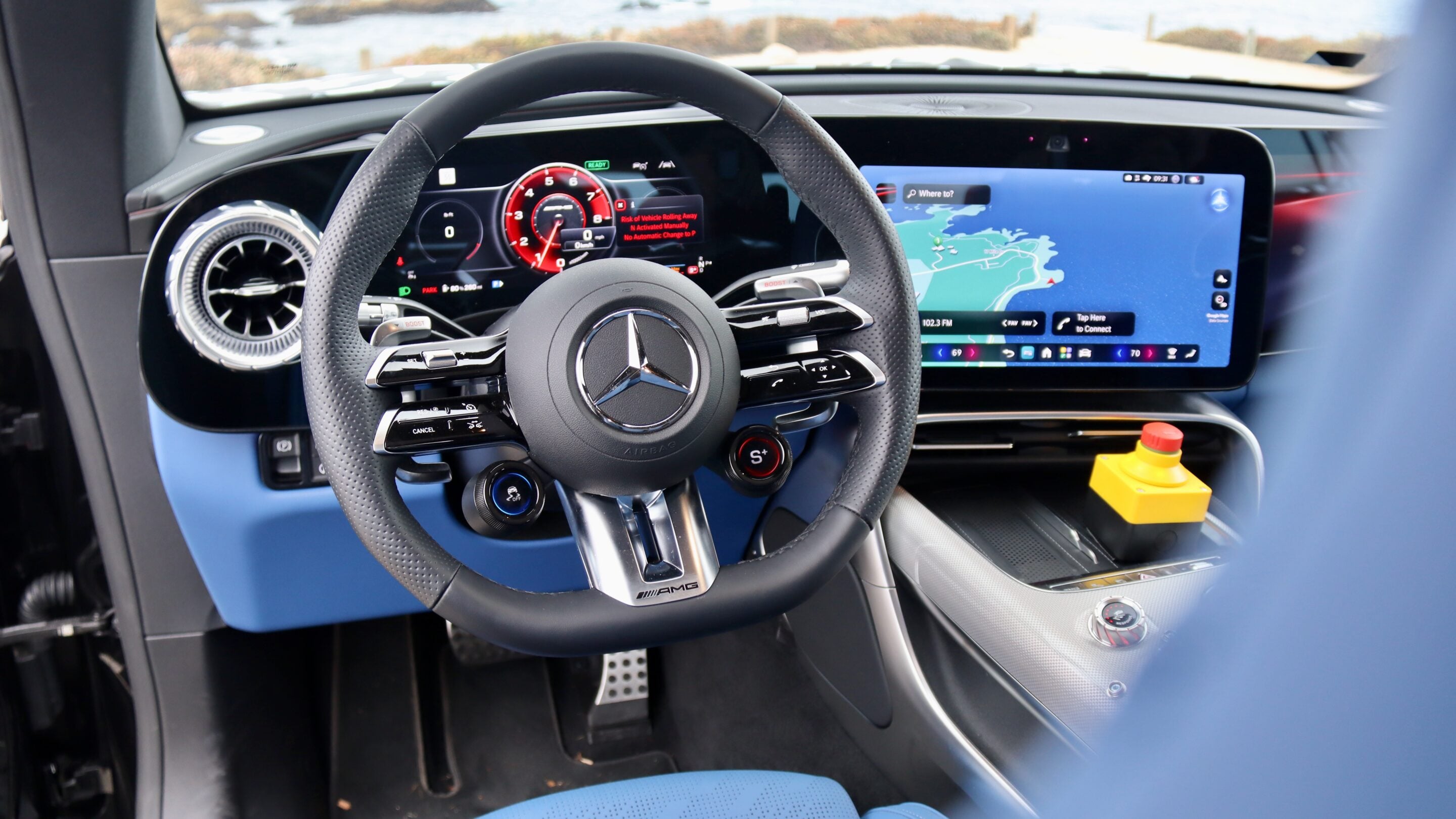 Close-up of a Mercedes-AMG car interior: steering wheel with AMG badge, digital instrument cluster, and a large map on the center touchscreen display.