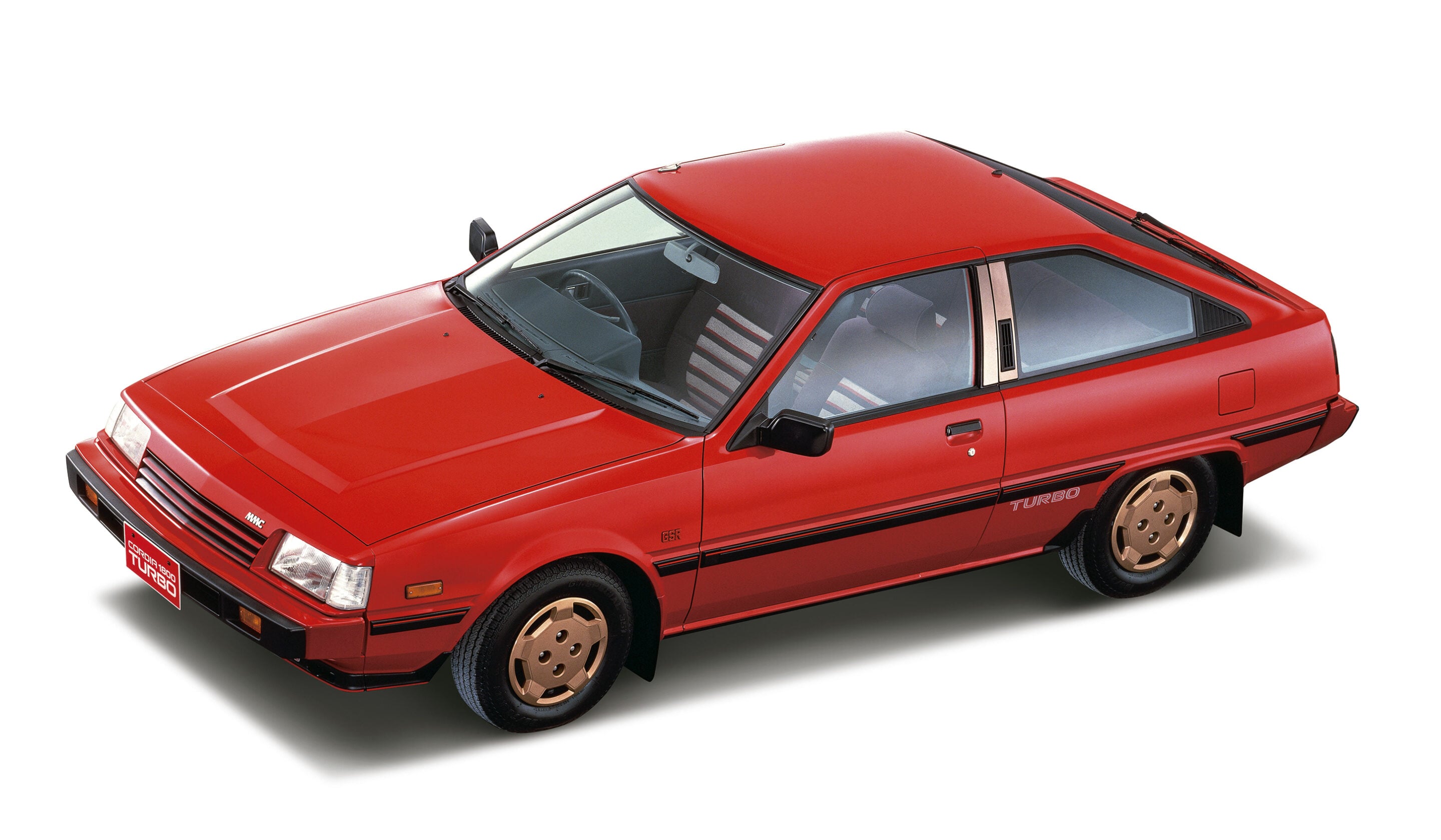 Red vintage sports car photographed from the front-left, featuring gold wheels and black trim, with a 'Turbo' badge along the side.