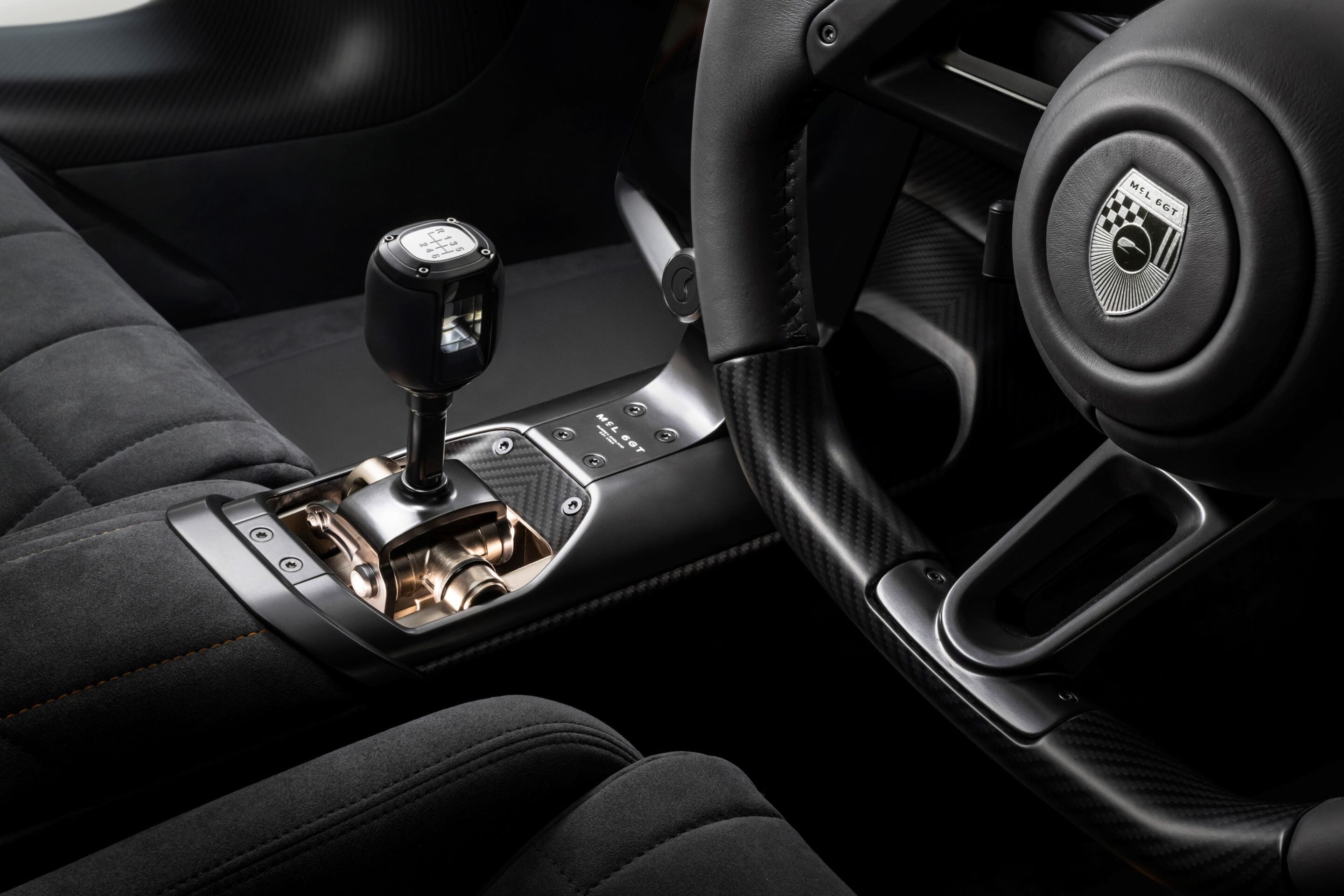 Close-up of a luxury car interior featuring a gated manual gear shifter, carbon fiber center console, and a steering wheel with a round badge