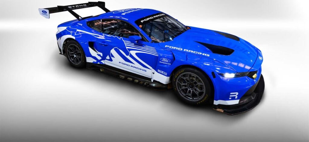 Blue Ford racing car with white graphics and a large rear wing, viewed from the front-right on a white studio background.