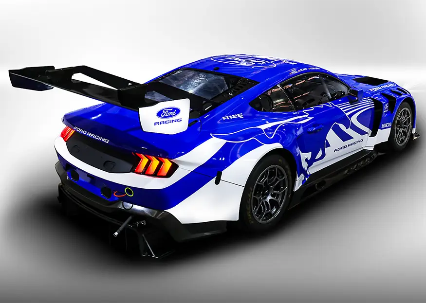 Rear three-quarter view of a blue Ford Racing race car with a large rear wing and white graphics against a light background