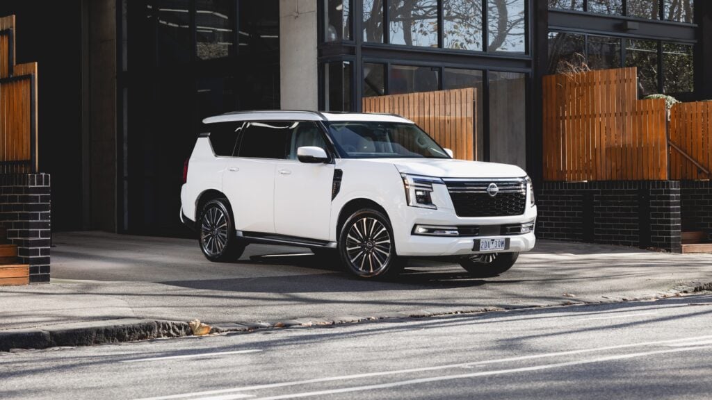 White Nissan SUV parked in front of a modern glass building with a wooden privacy fence.