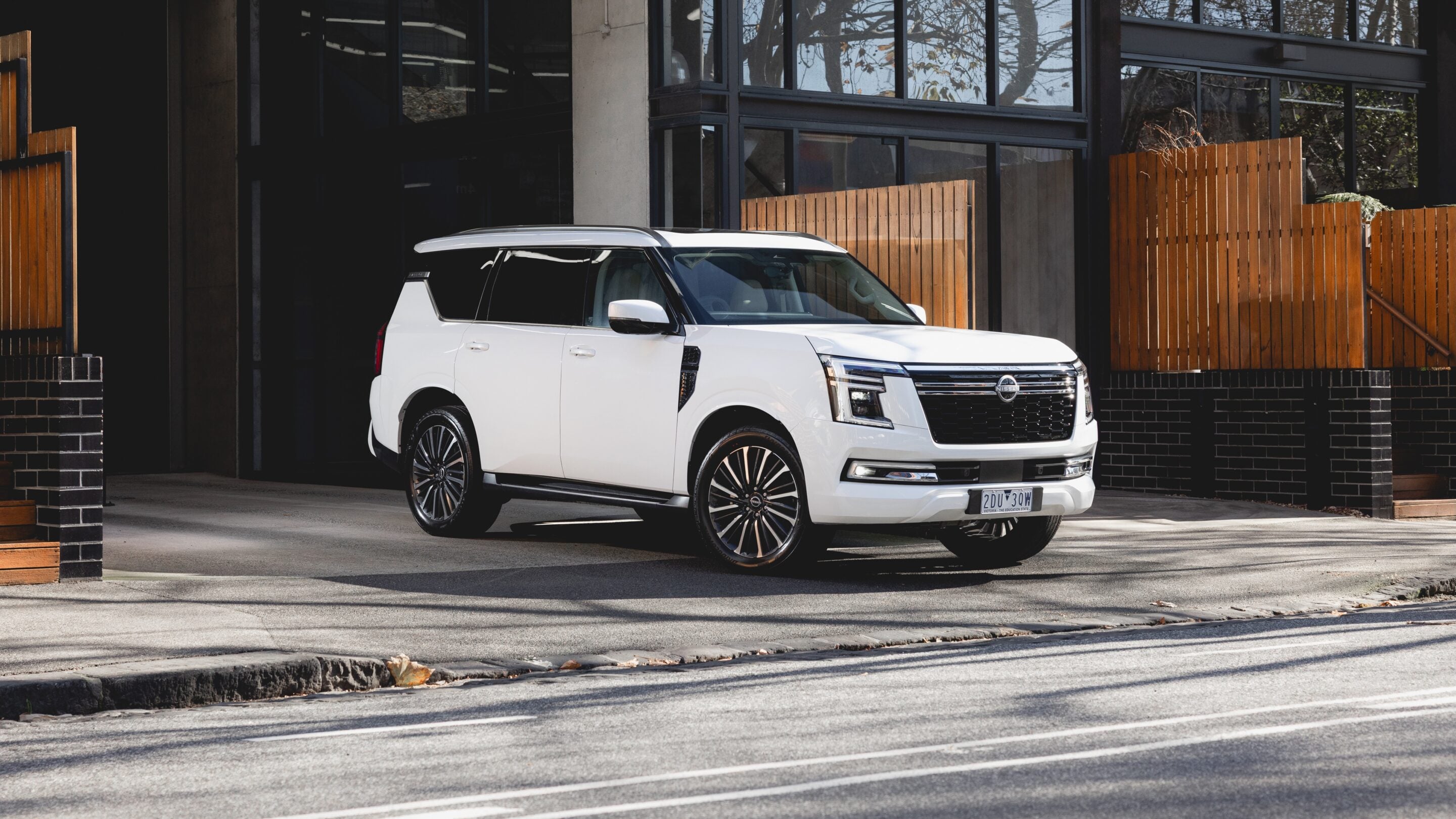 White Nissan SUV parked in front of a modern glass building with a wooden privacy fence.
