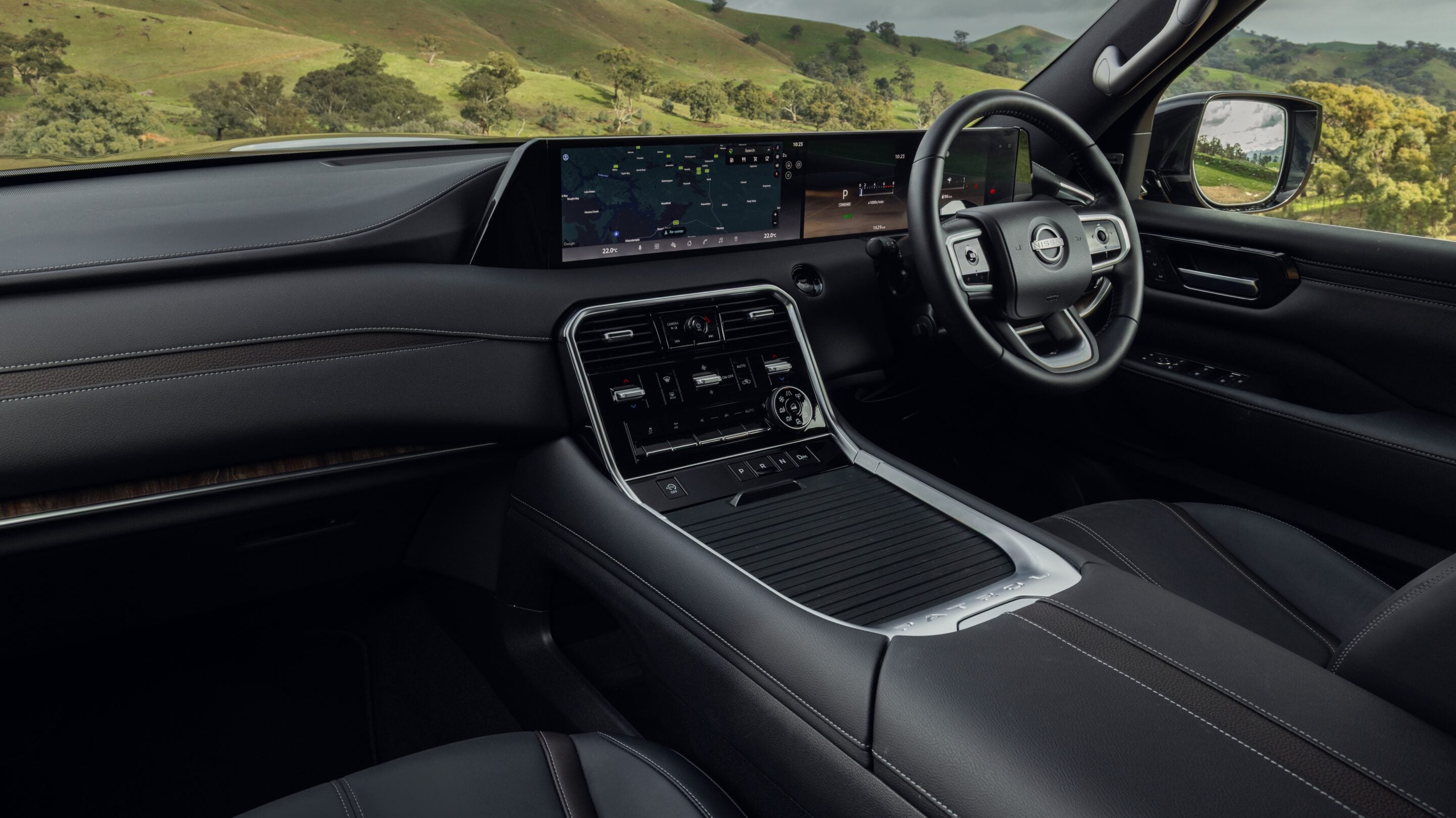 Interior of a luxury SUV with a wide digital dashboard, steering wheel, and chrome center console; countryside visible through the windshield.