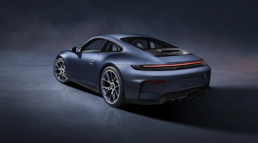 Blue sports car photographed from the rear three-quarter view on a dark studio floor.