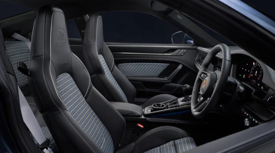 Interior of a Porsche: black leather sport seats with blue plaid fabric, center console, and steering wheel.
