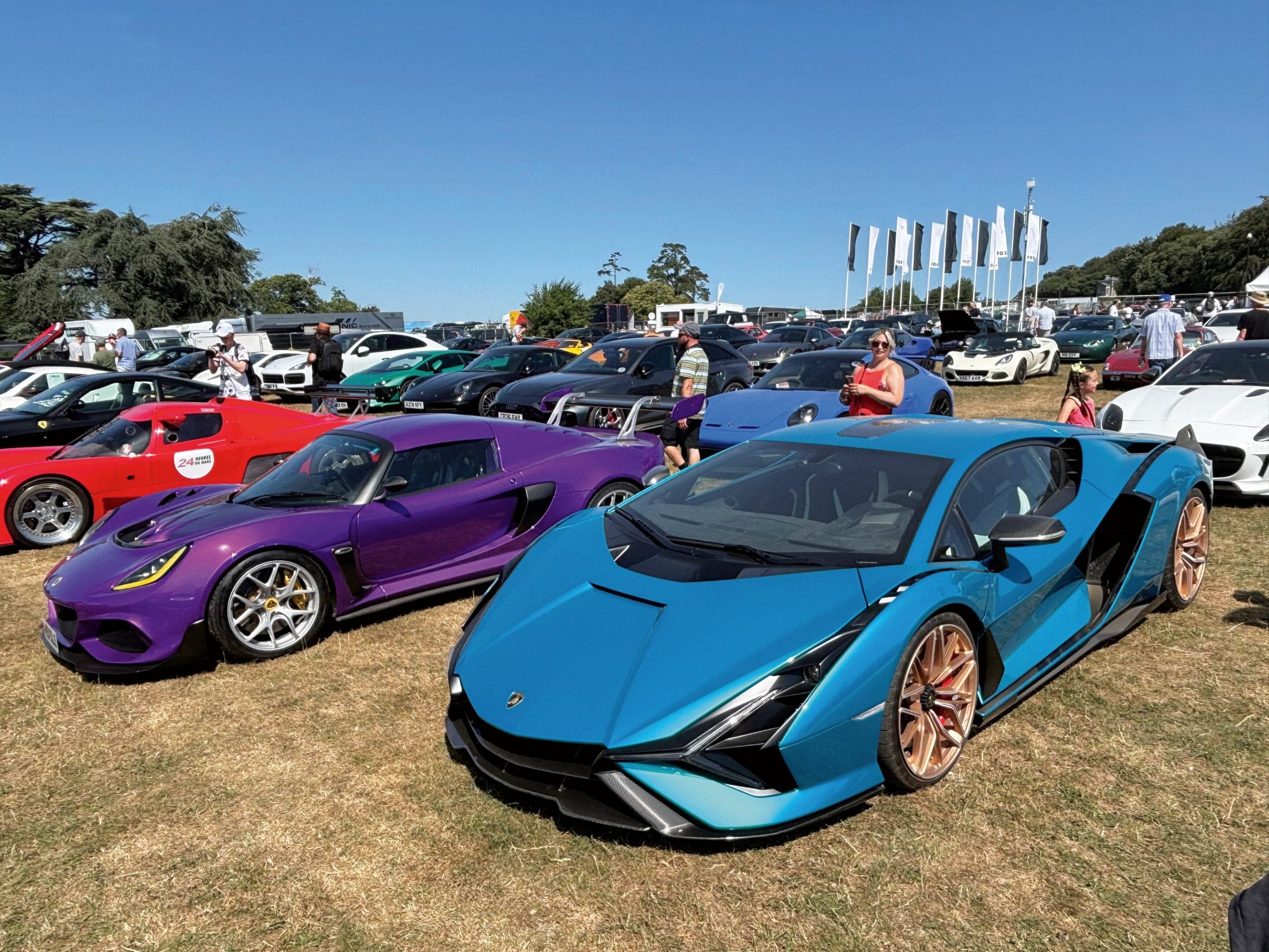 Row of bright sports cars parked on a sunny day at an outdoor car show with people walking between them