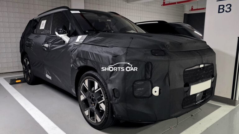 Camouflaged SUV prototype parked in a garage; black wrap conceals design, Shorts Car watermark visible.