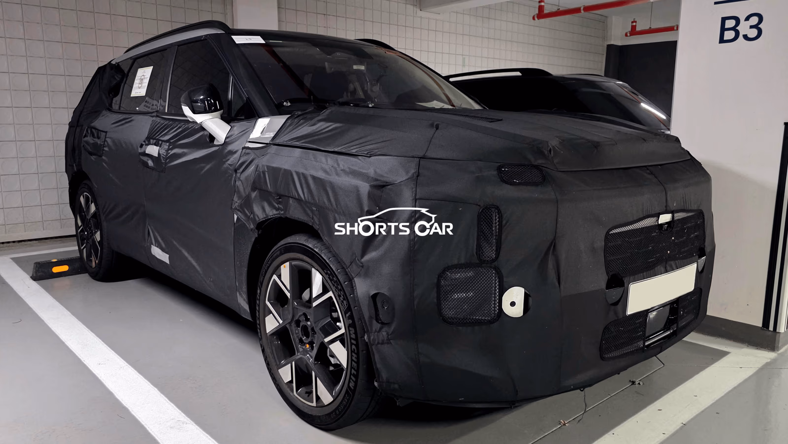 Camouflaged SUV prototype parked in a garage; black wrap conceals design, Shorts Car watermark visible.