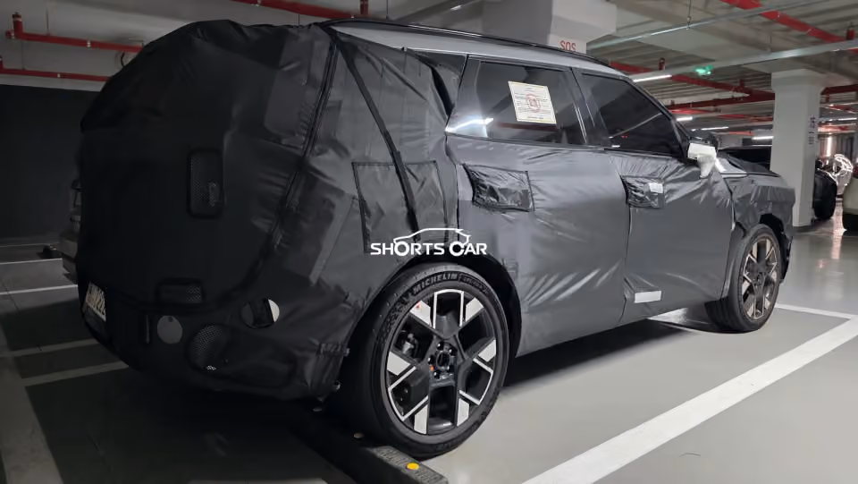Camouflaged prototype SUV covered with a dark protective wrap in a parking garage.