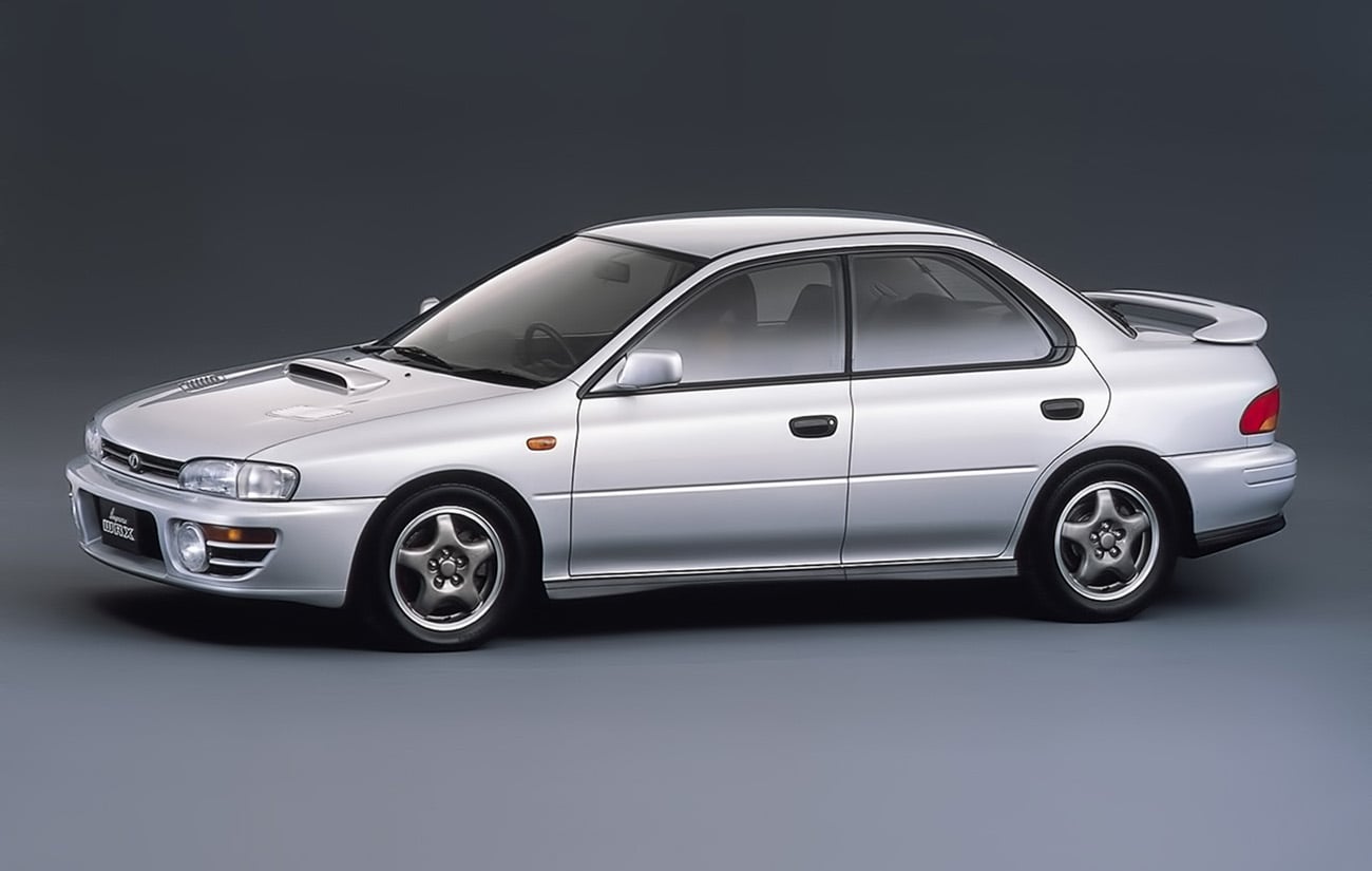 Silver Subaru WRX sedan seen from the side with hood scoop and rear spoiler.