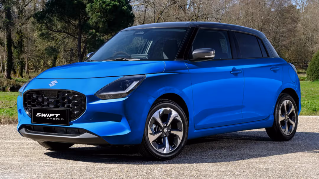 Blue Suzuki Swift Hybrid shown from a front-right three-quarter view parked on a paved road with trees in the background.