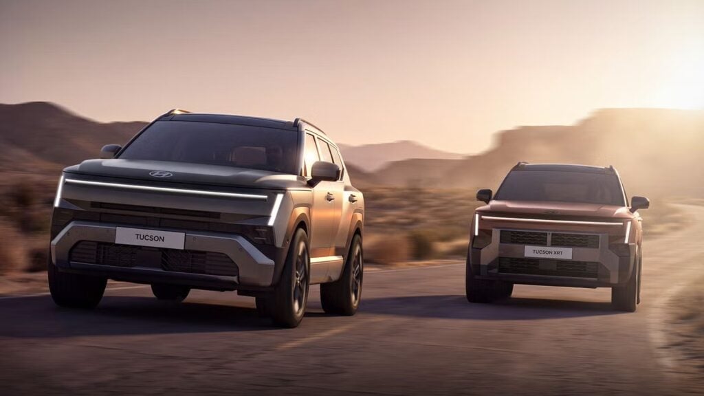 Two modern SUVs drive side by side on a desert highway at sunset, rugged mesas in the distance.