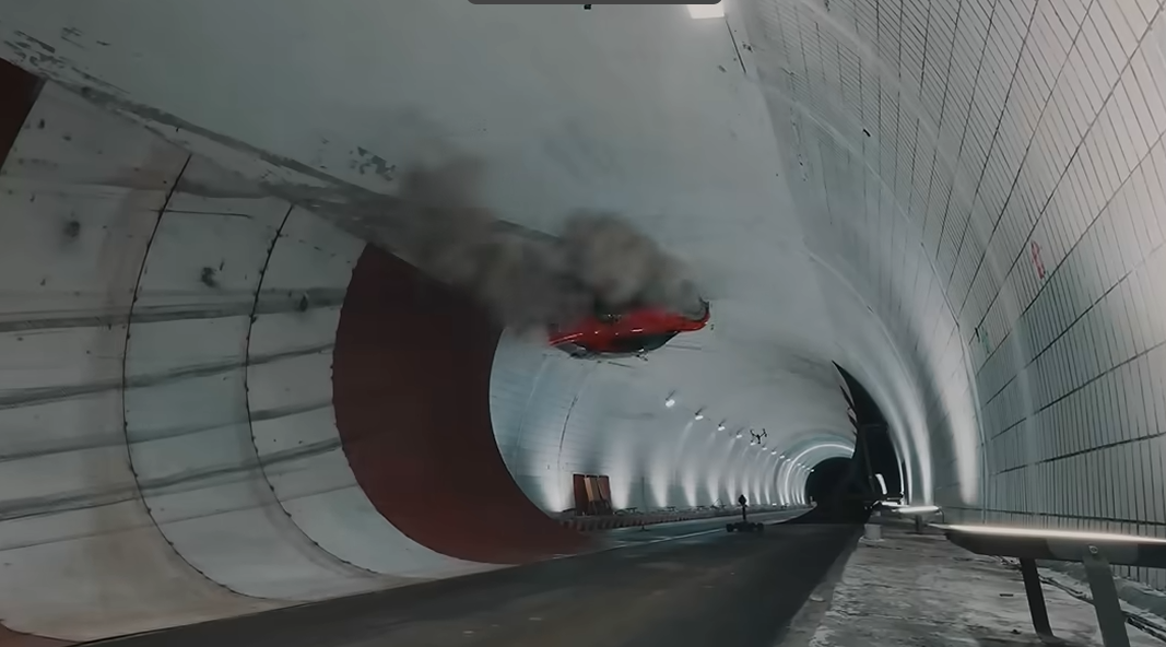 Red car suspended in mid-air inside a long, curved, white-tiled tunnel with smoke trailing behind.