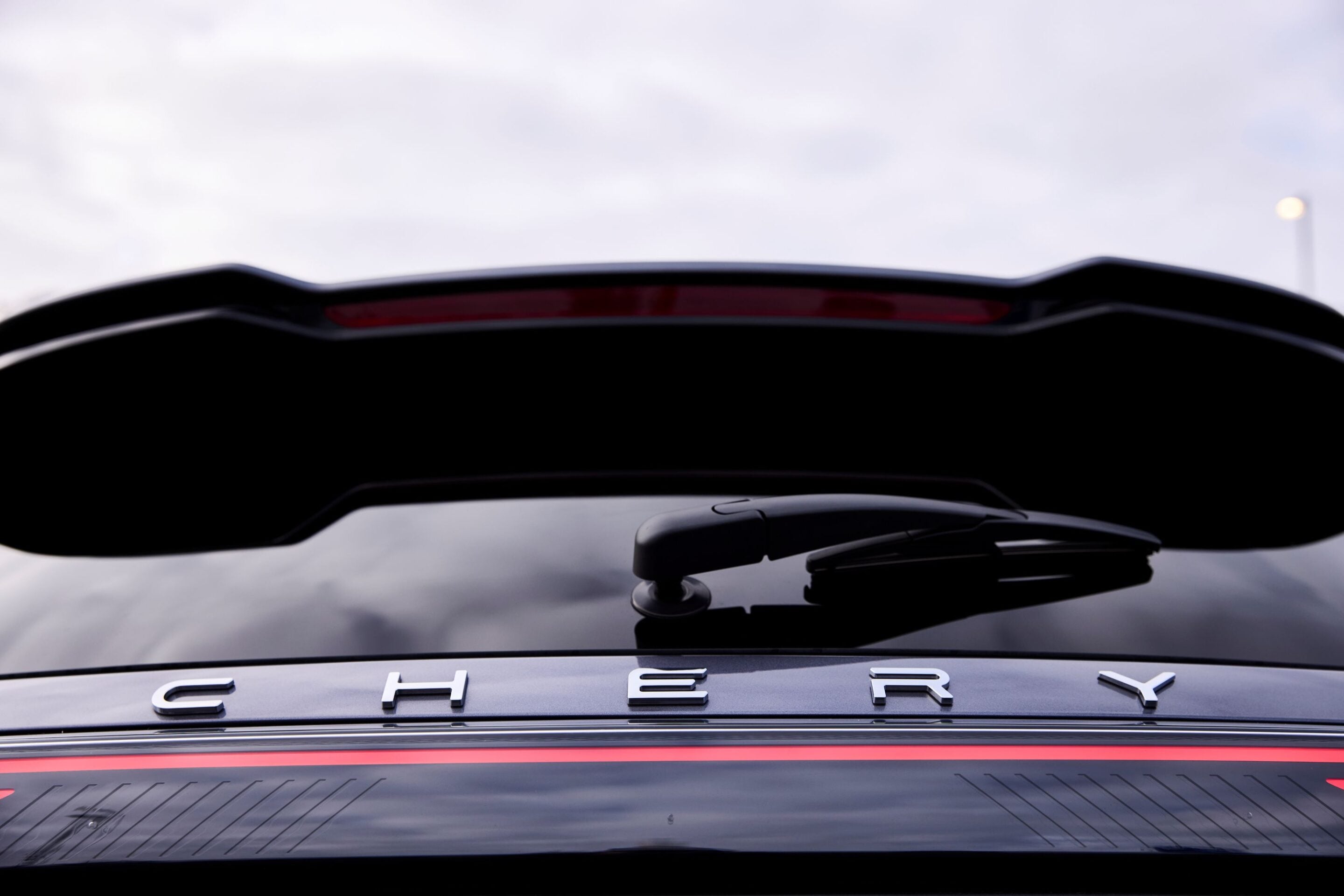 Rear view of a dark car showing the CHERY letters on the trunk and a red taillight strip above the bumper