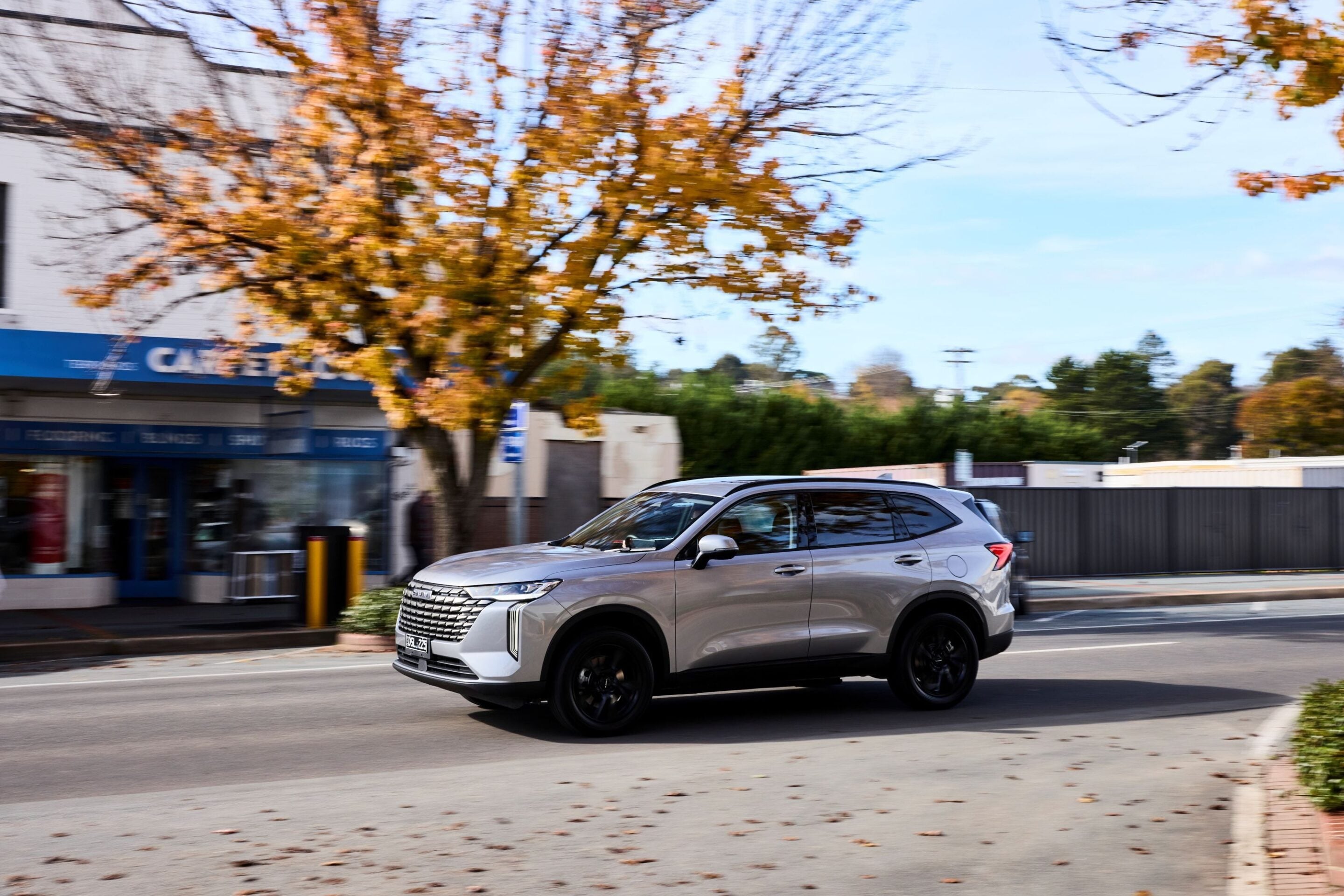 Silver SUV driving down a city street with autumn-colored trees and a storefront in the background