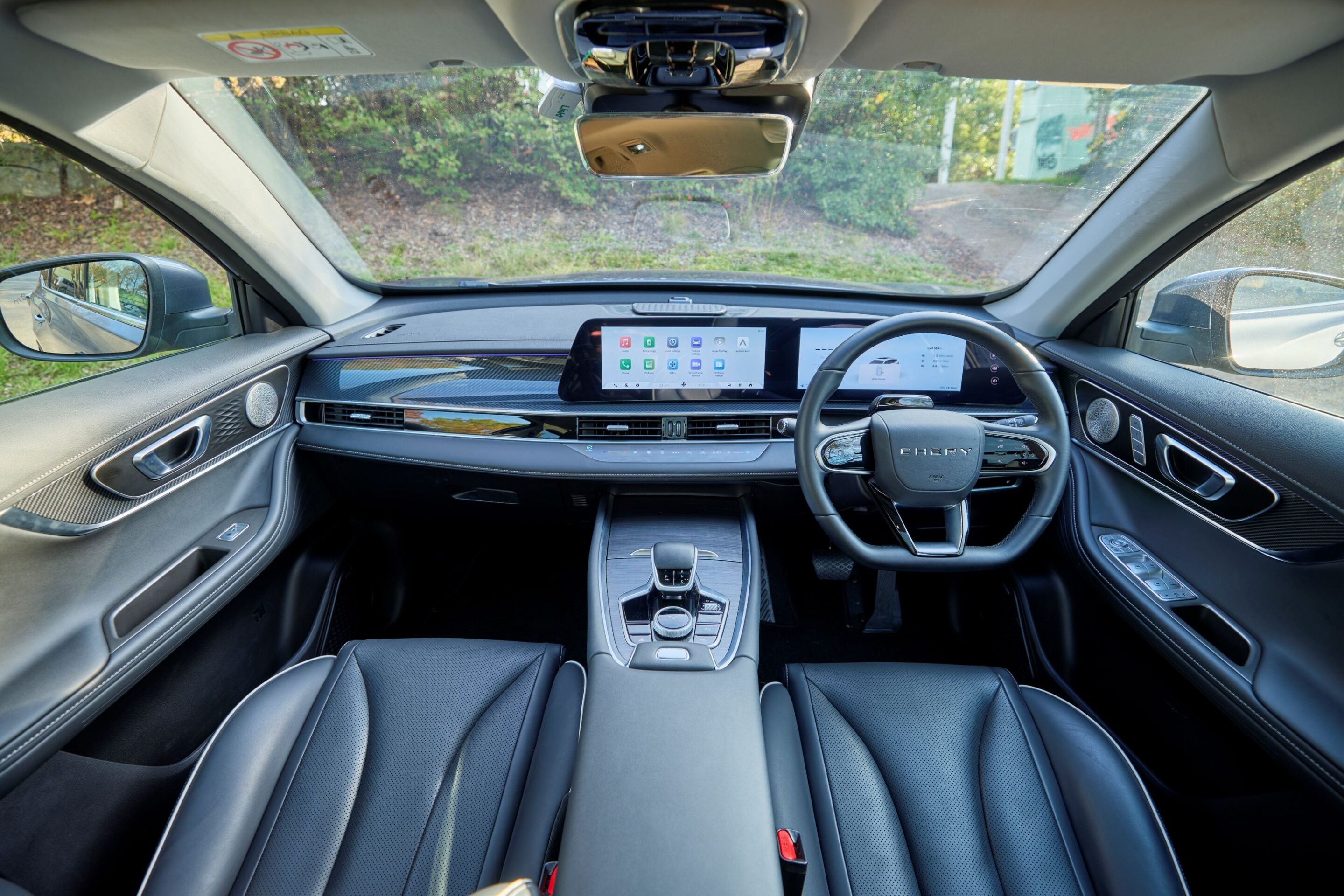 Inside a modern luxury car cabin viewed from the front passenger seat, featuring a wide central touchscreen and sleek center console.