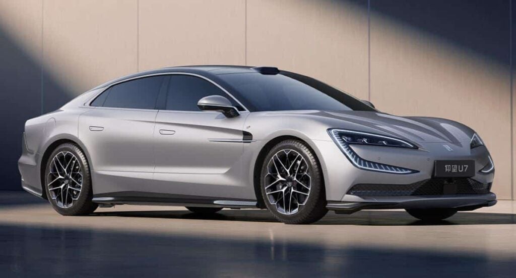 Silver luxury sedan parked outdoors, viewed from the front-right with sleek LED headlights and large multi-spoke wheels.