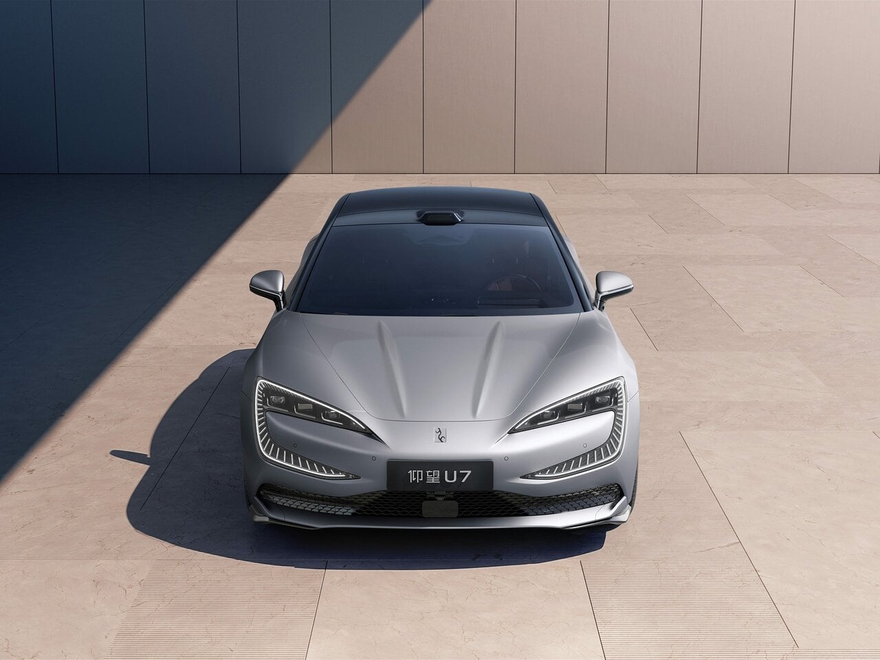 Front view of a sleek silver luxury car parked on a pale stone plaza, with sharp LED headlights and a wide black grille.