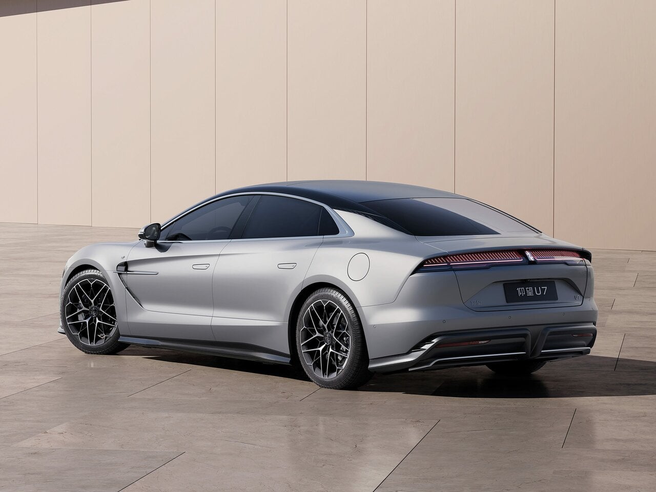 Silver four-door luxury sedan seen from the rear three-quarter, parked on a light tiled surface against a beige wall.