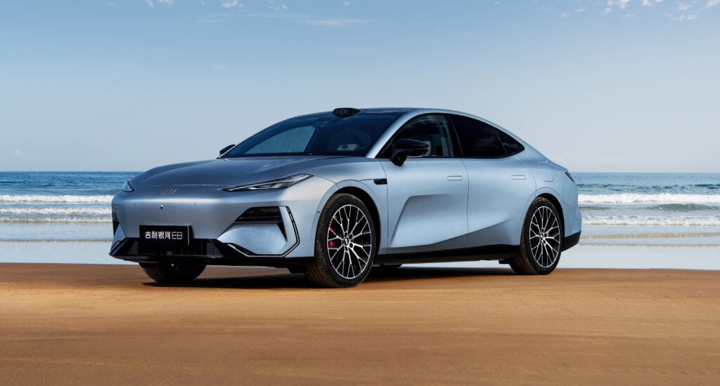 Silver modern sedan parked on a sandy beach with the ocean in the background.