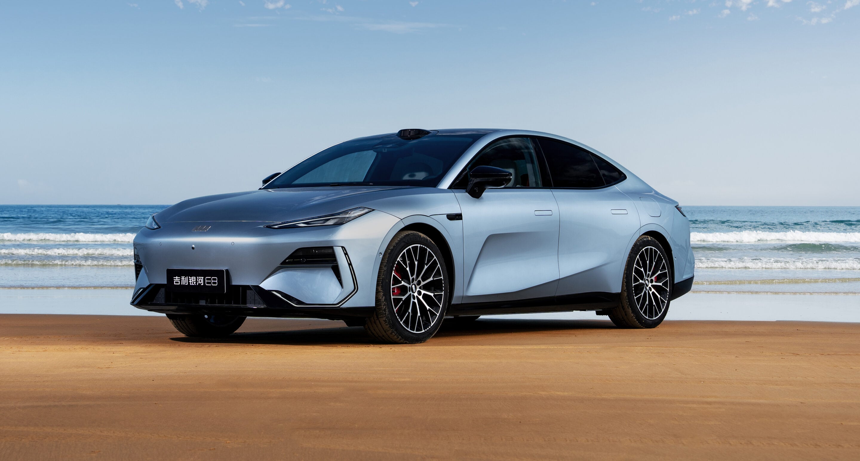 Silver modern sedan parked on a sandy beach with the ocean in the background.