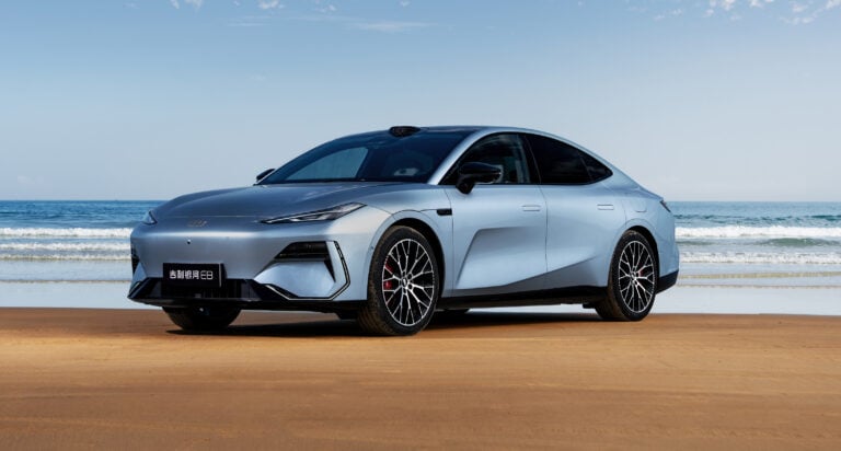 Silver modern sedan parked on a sandy beach with the ocean in the background.