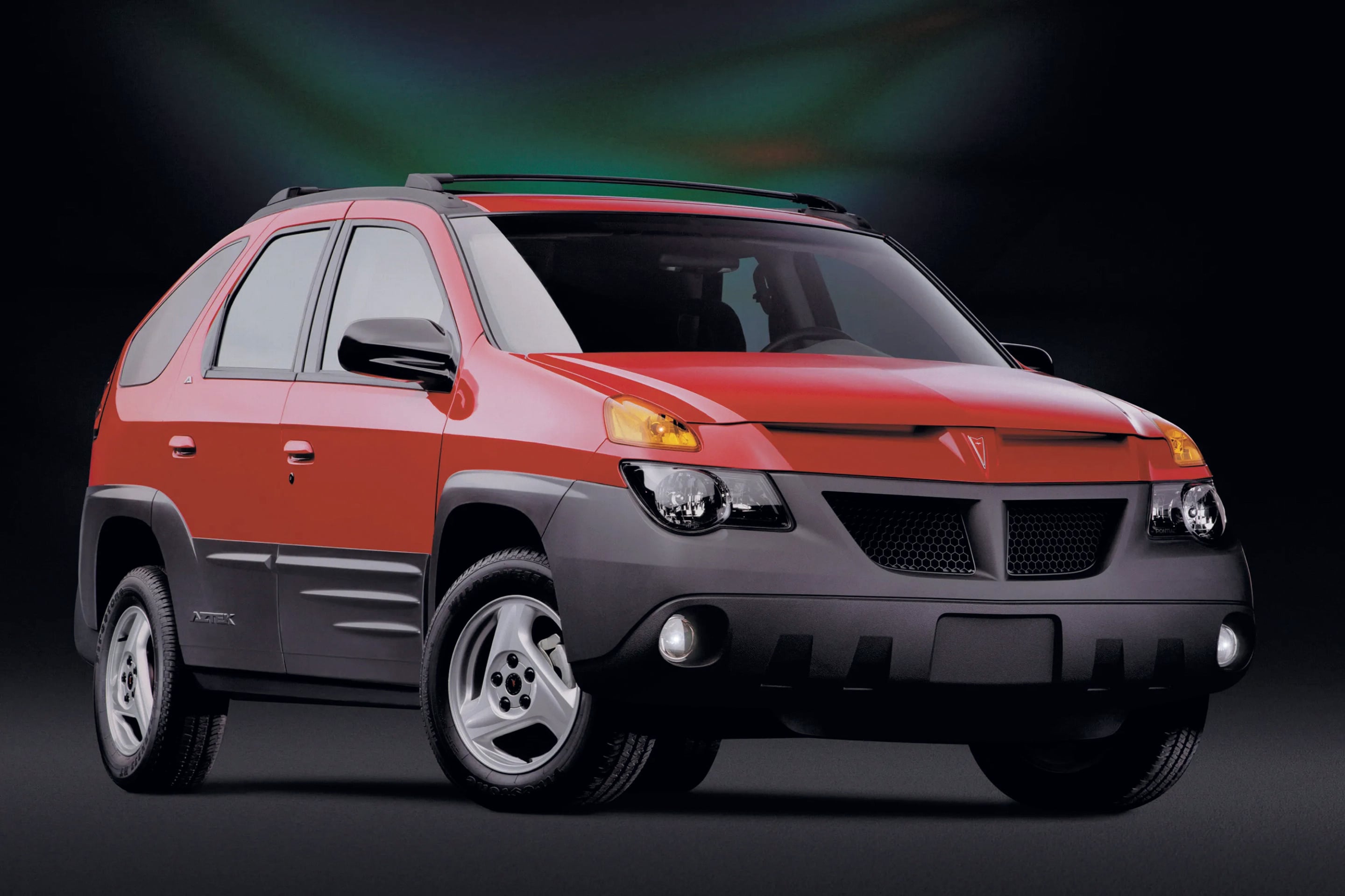 Red/pink SUV shown from the front-left, featuring roof rails and sporty grille against a dark backdrop, partial view of wheels.