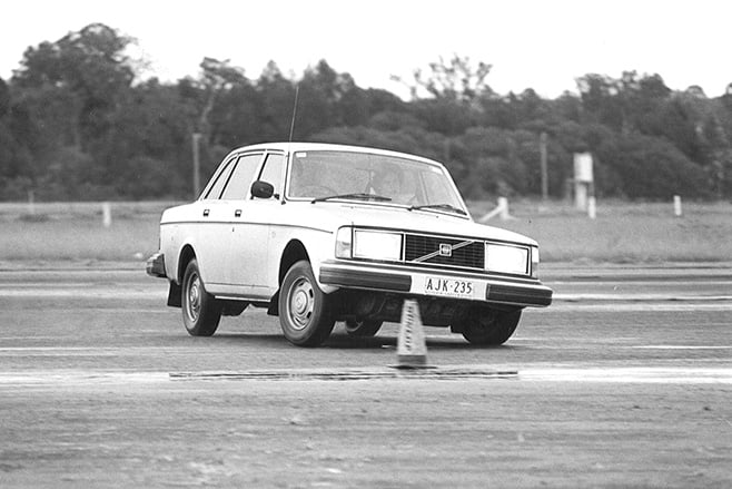 White Volvo sedan maneuvering around a traffic cone on an empty driving test track (black-and-white photo)