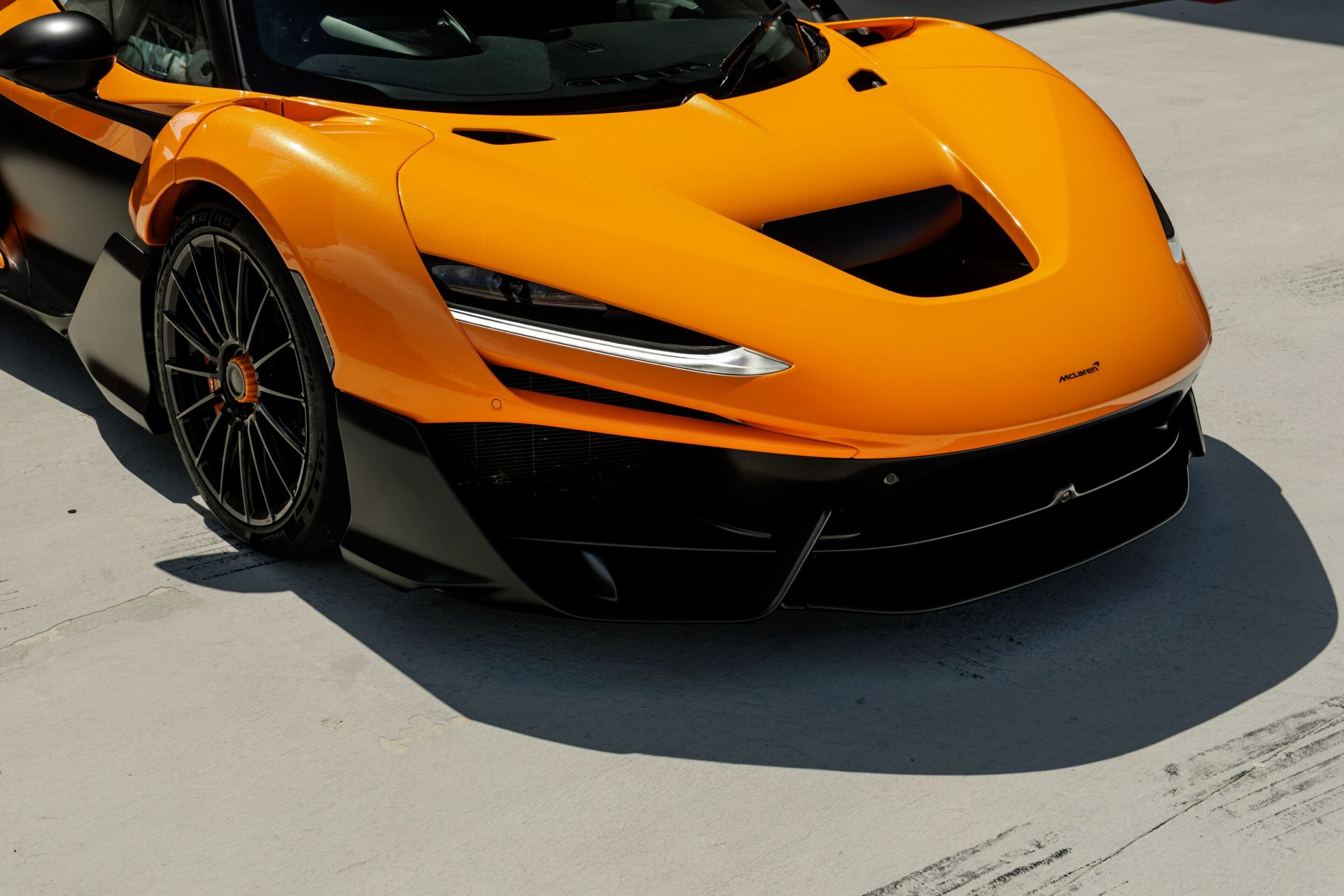 Bright orange McLaren sports car front end with large air intake and black wheel detail