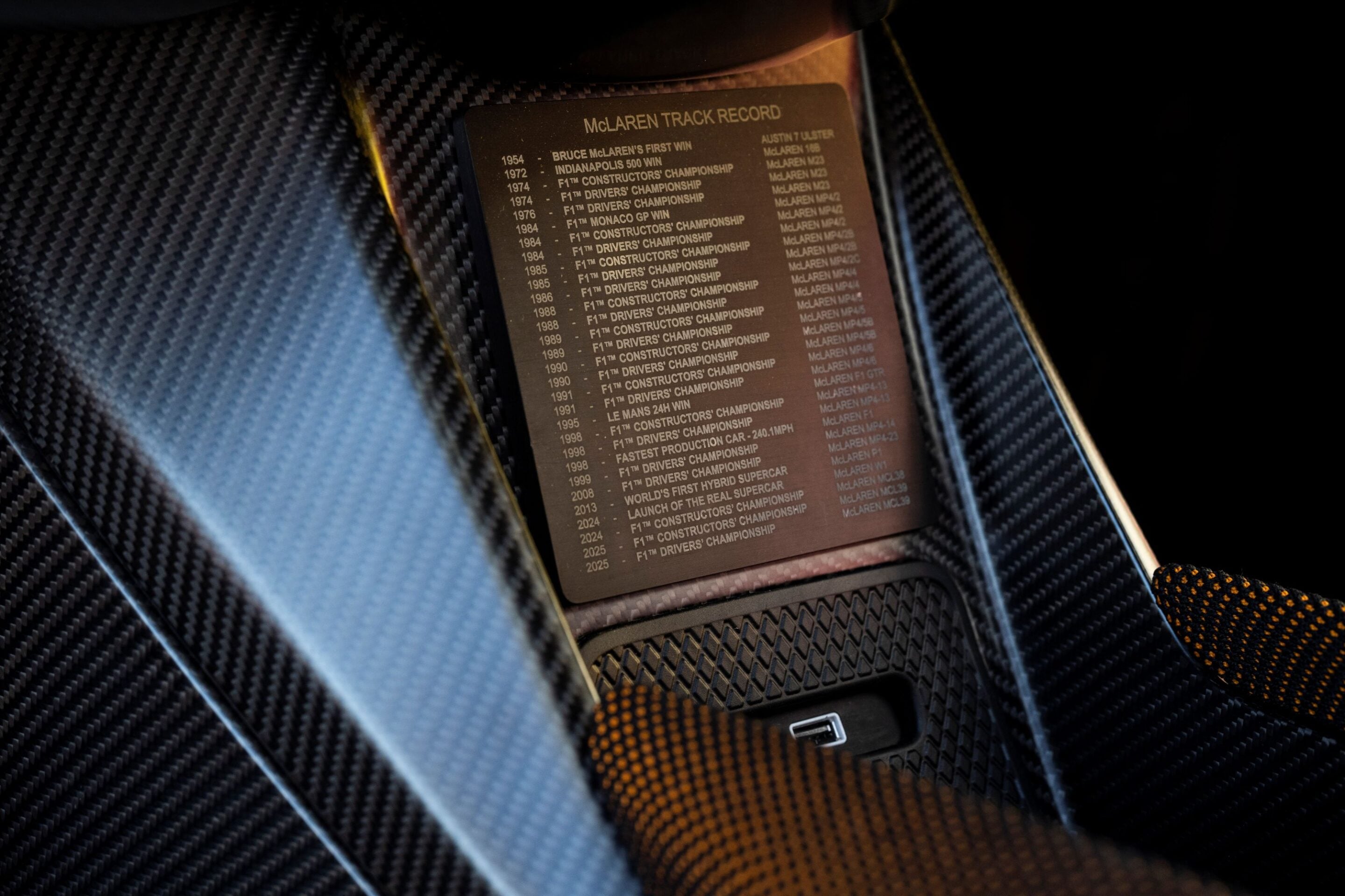 Bronze plaque reading 'McLAREN TRACK RECORD' mounted on carbon fiber background, listing racing years and wins/achievements (McLaren)