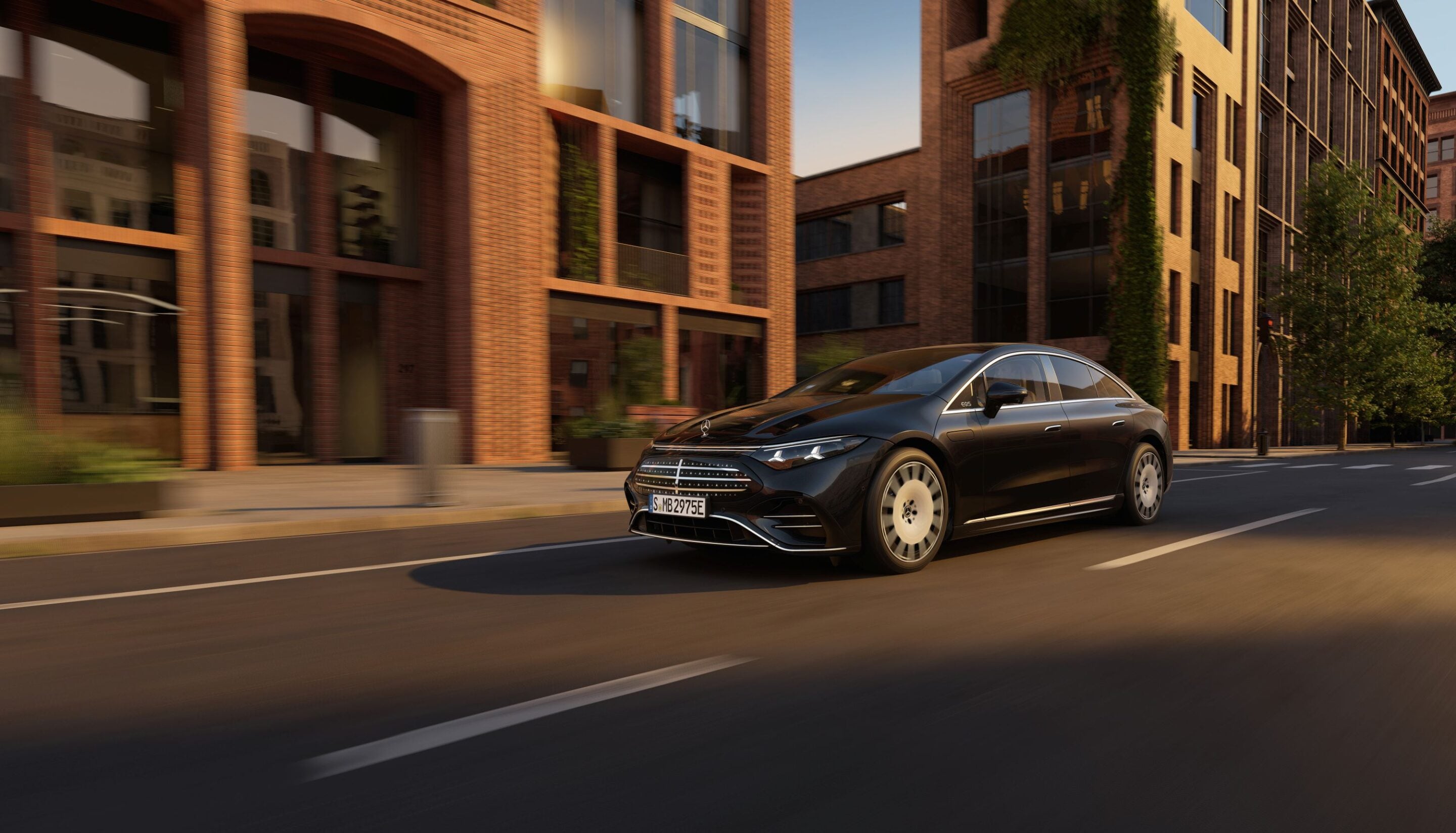 Black luxury sedan driving on a city street with brick buildings and motion blur on the road behind it.