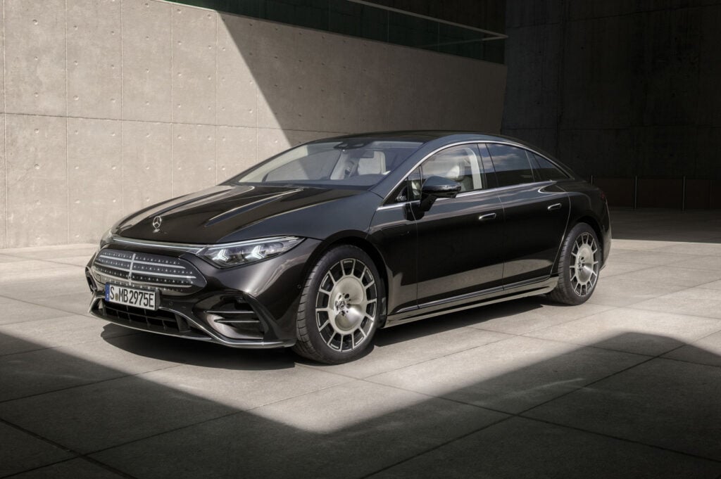 Black Mercedes-Benz sedan parked on light-gray tiles beside a concrete wall, with a diagonal shadow crossing the scene.