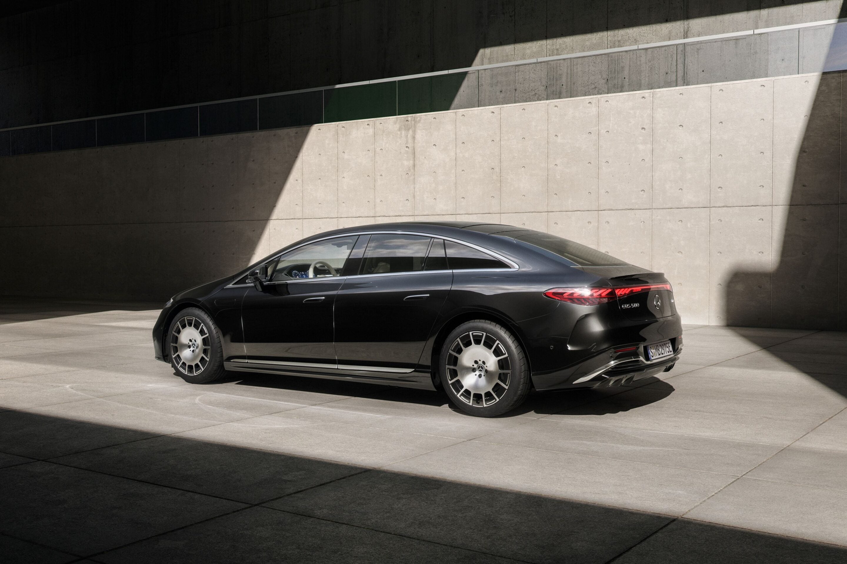 Black luxury sedan parked along a concrete wall with dramatic shadows across the scene.