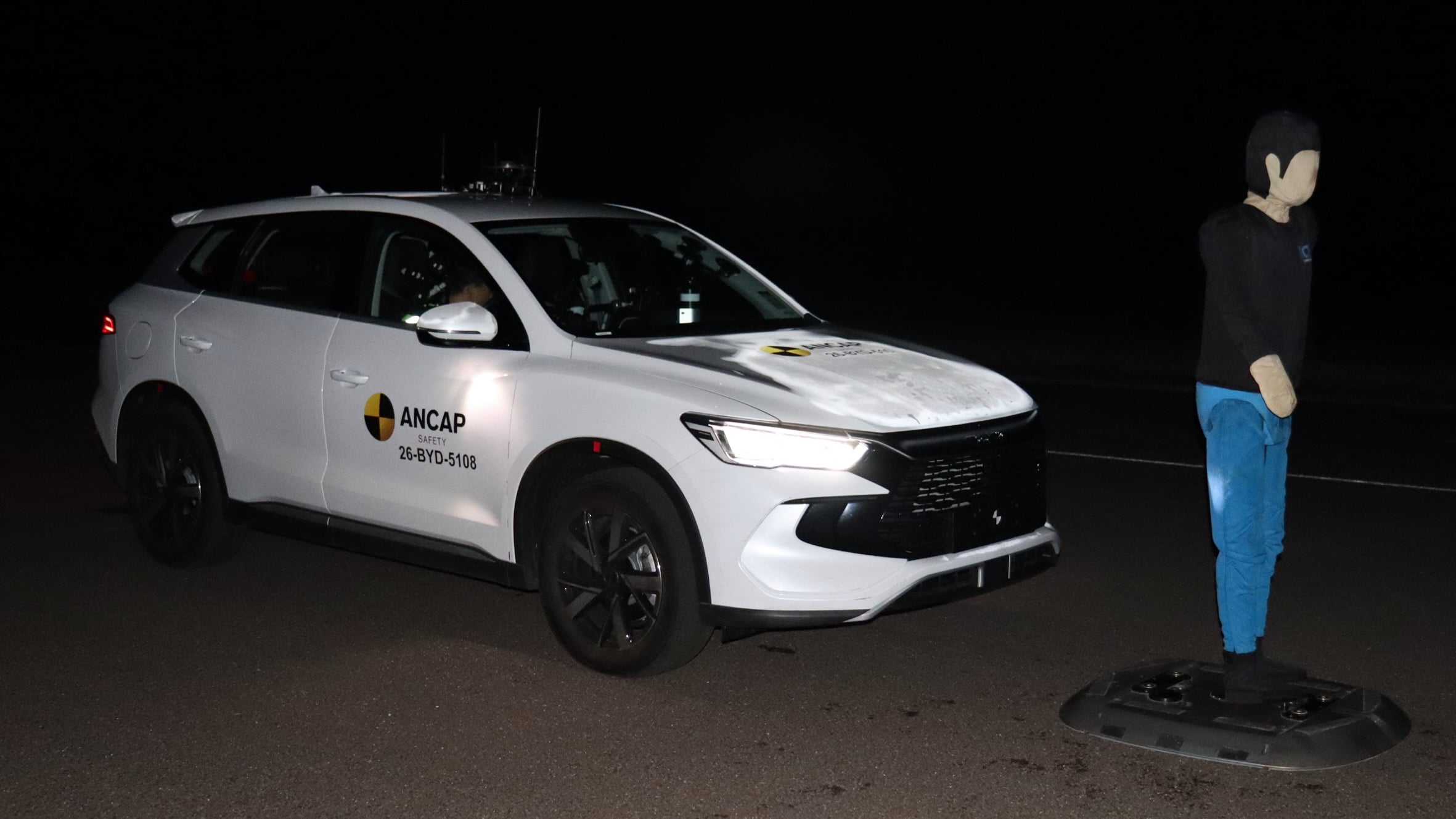White ANCAP safety SUV at night with a person wearing a balaclava standing nearby.