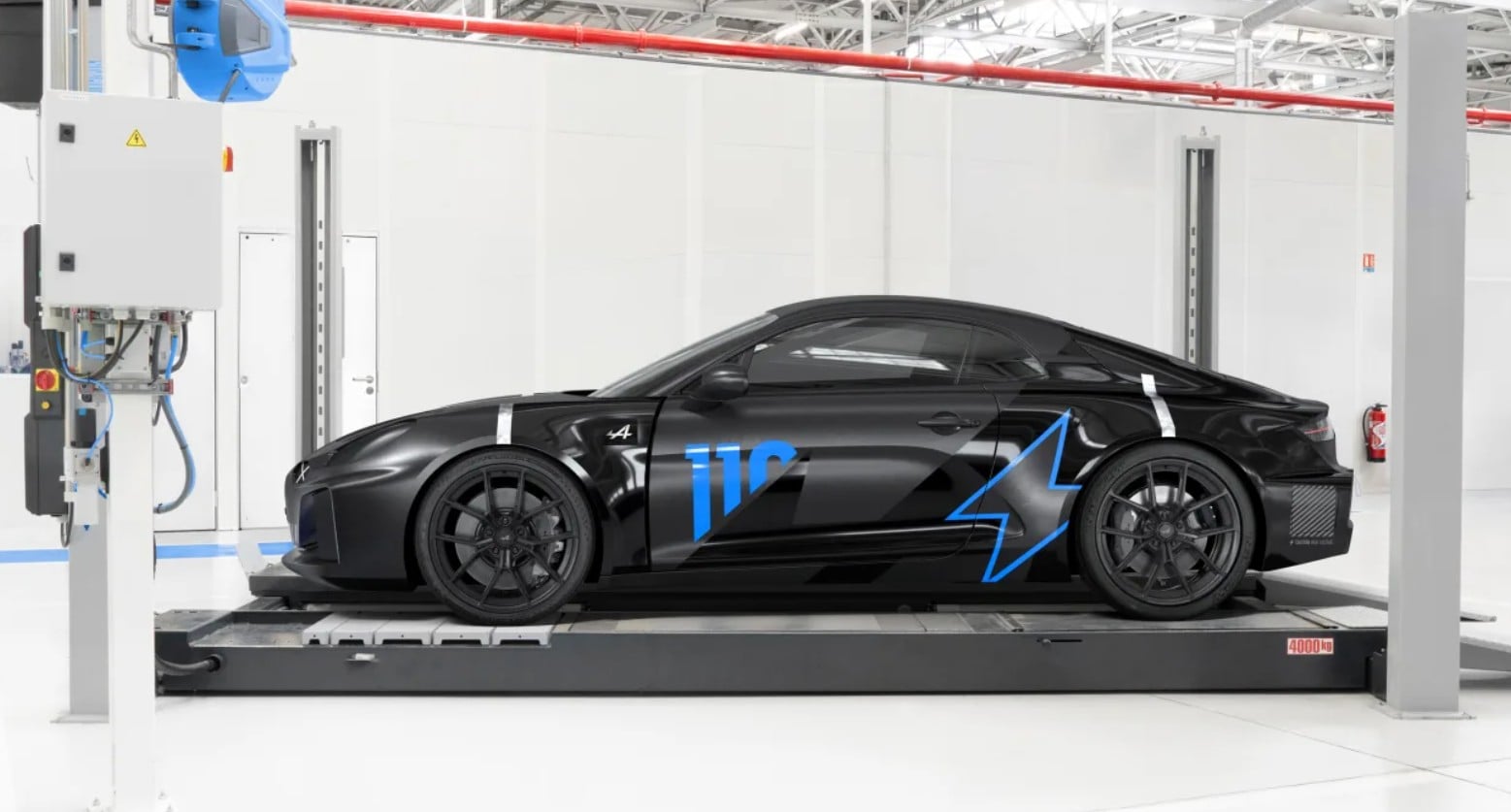 Black sports car with blue graphics on a lift in a bright automotive workshop.