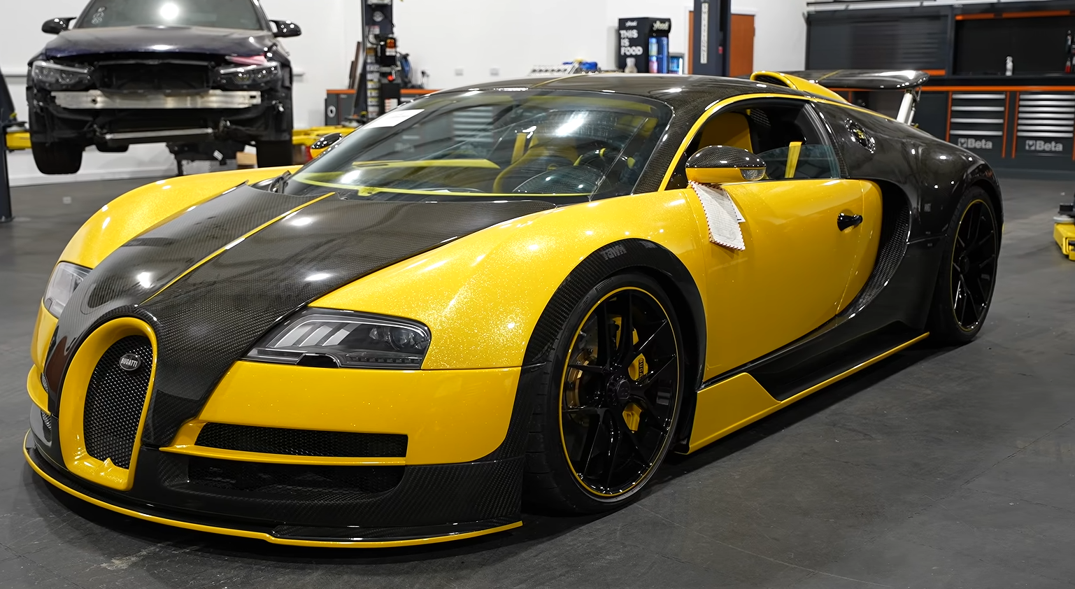 Yellow Bugatti Veyron with black carbon fiber roof in a garage showroom
