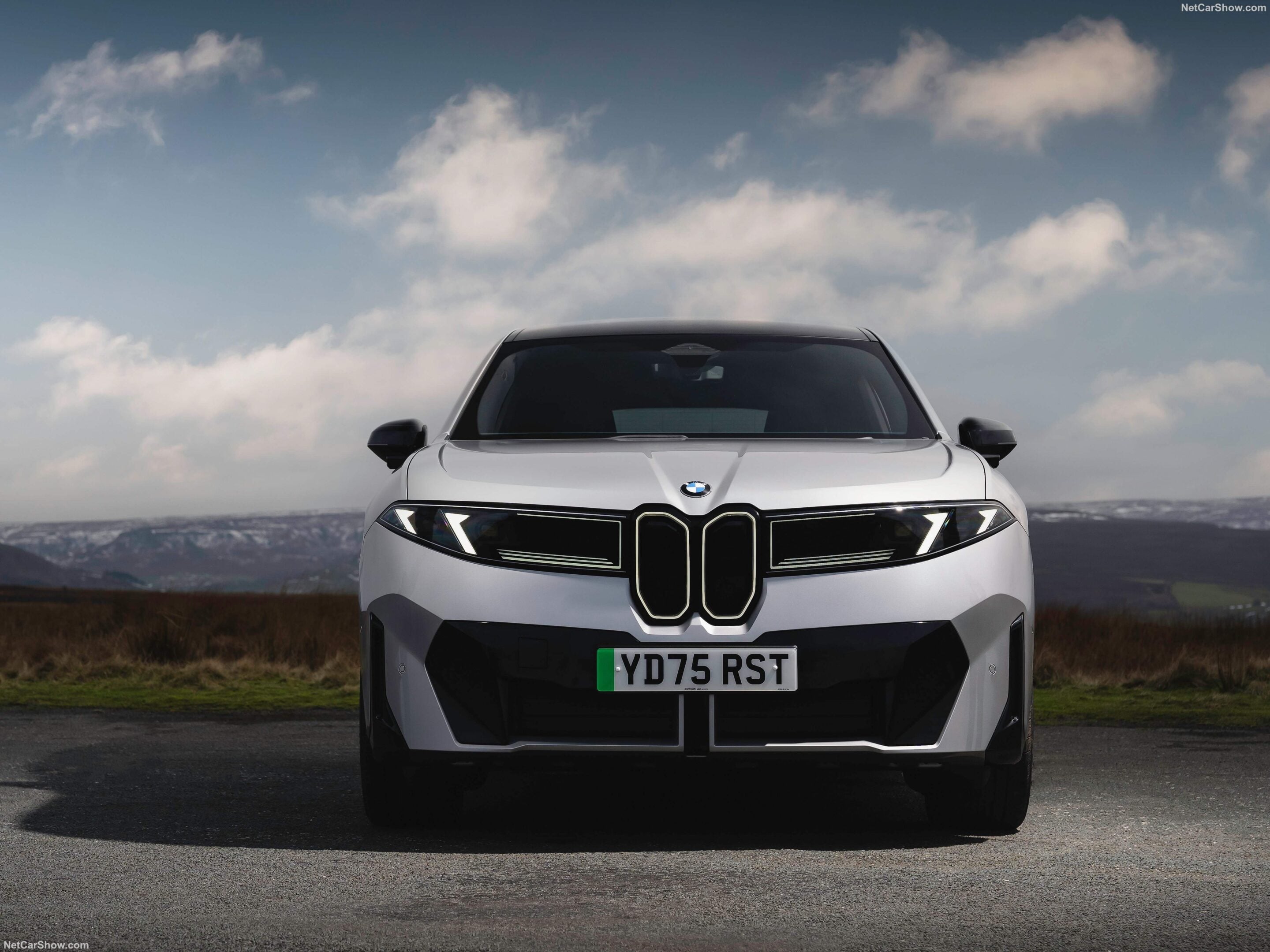 Front view of a white BMW SUV facing the camera, with the license plate YD75 RST and a cloudy blue sky in the background.
