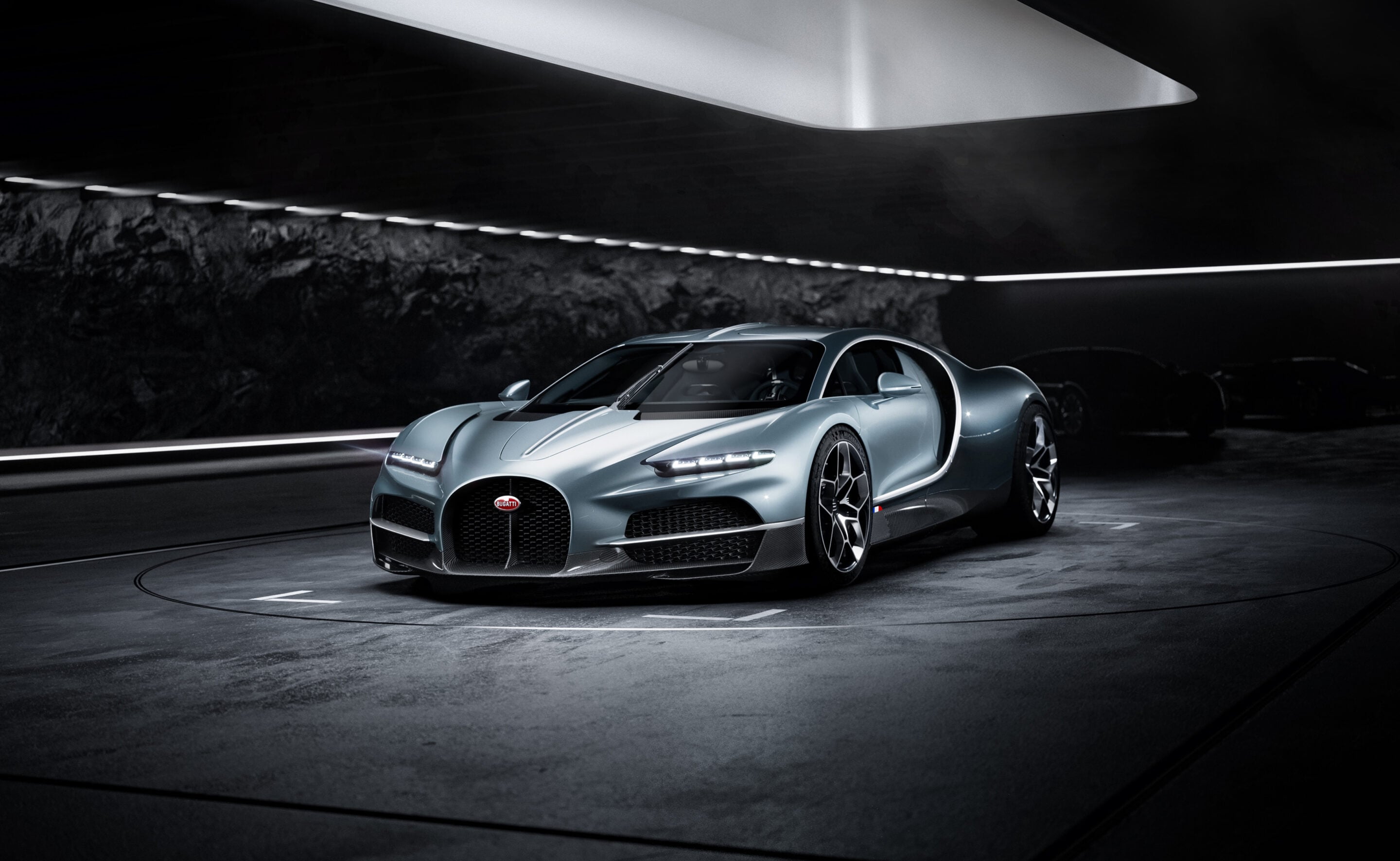 Blue Bugatti hypercar in a dark underground showroom, shown from a front three-quarter angle with dramatic lighting.