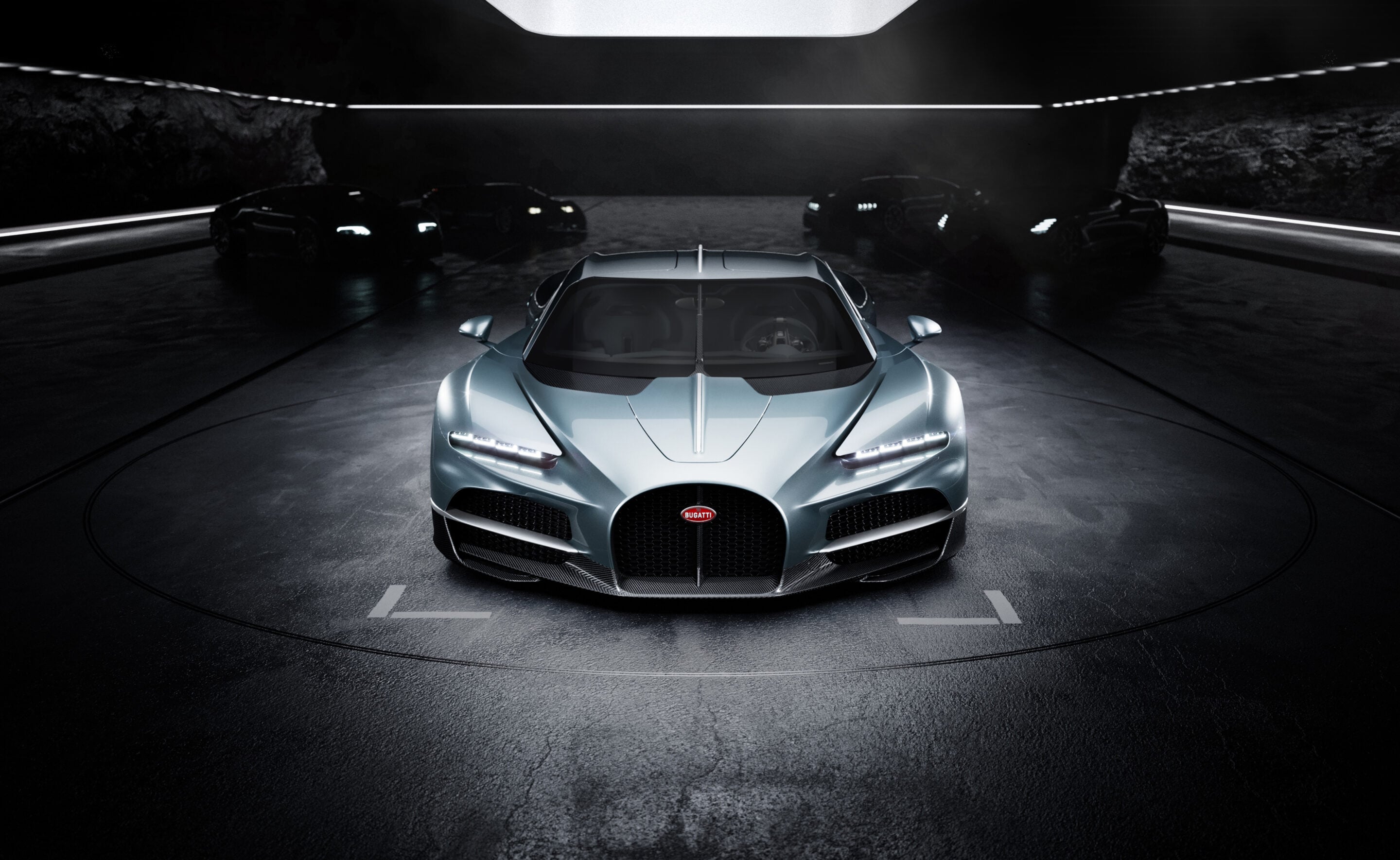 Front view of a silver Bugatti sports car in a dark showroom tunnel with other cars in the background, dramatic lighting.