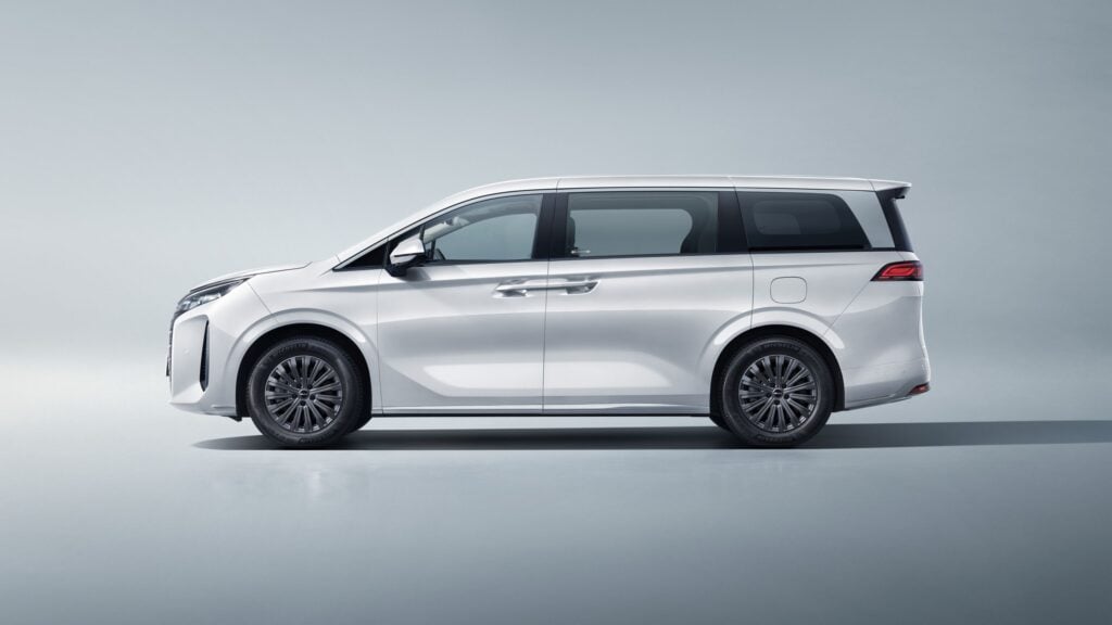 Side view of a silver/white minivan with tinted windows and alloy wheels against a pale gradient backdrop.