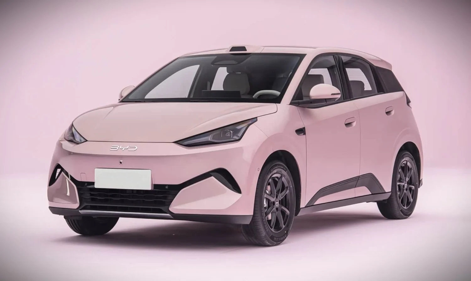 Pink BYD compact hatchback photographed in a studio, three-quarter front view with soft pink background.