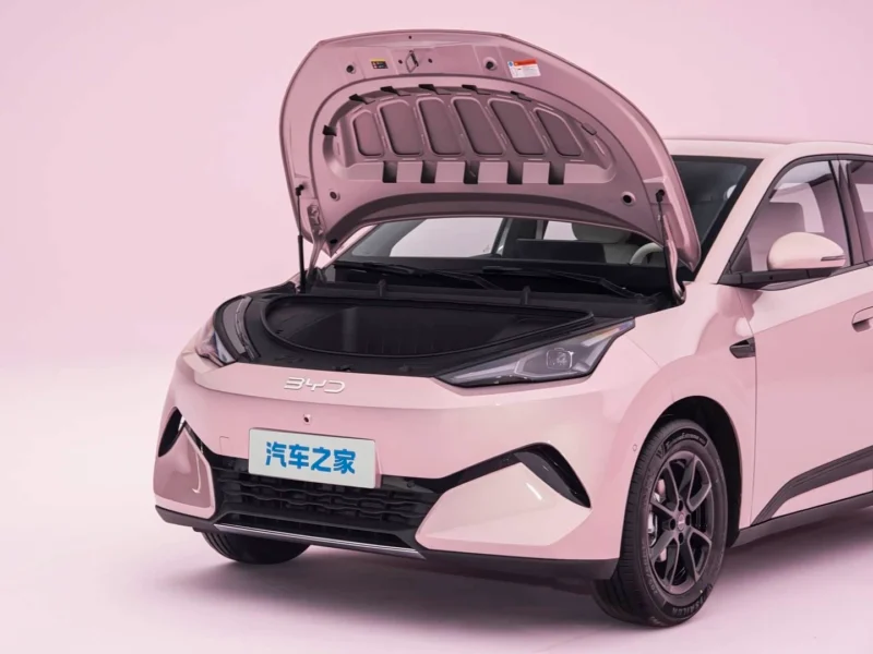 Pink BYD sedan with its hood raised, showing the engine bay in a studio setting with a blue Chinese license plate.