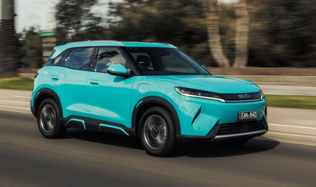 Turquoise BYD SUV driving quickly on a highway, motion blur in the background and foreground edges imply high speed.