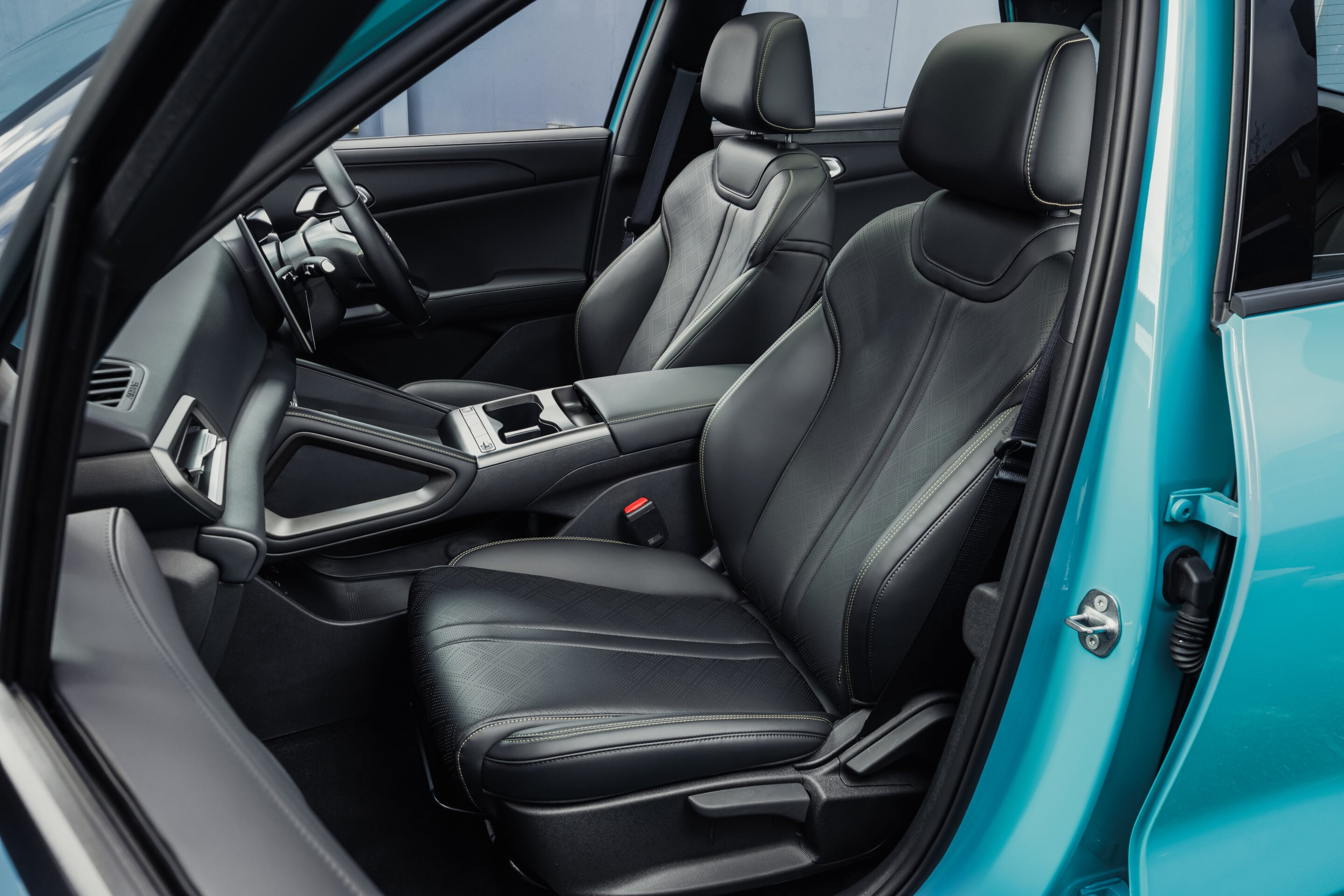 Open car door revealing the black leather interior with two front bucket seats in a teal car.